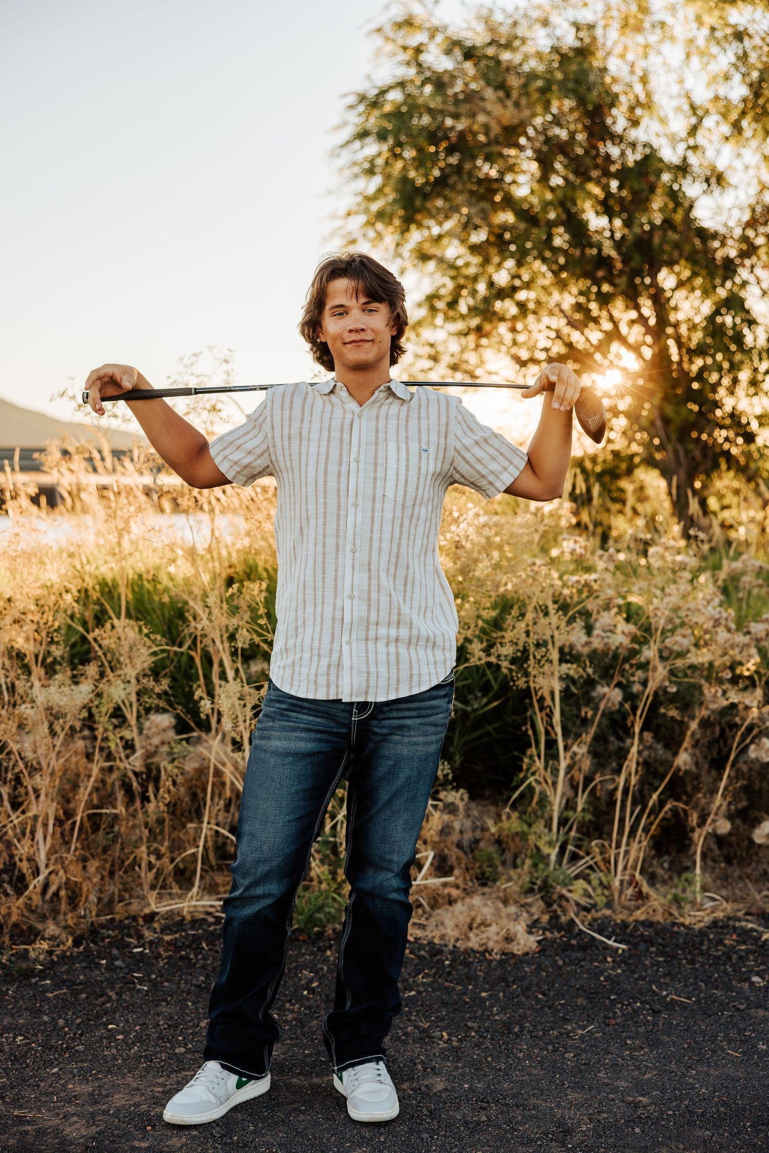 Person in striped shirt and jeans posing outdoors during sunset.