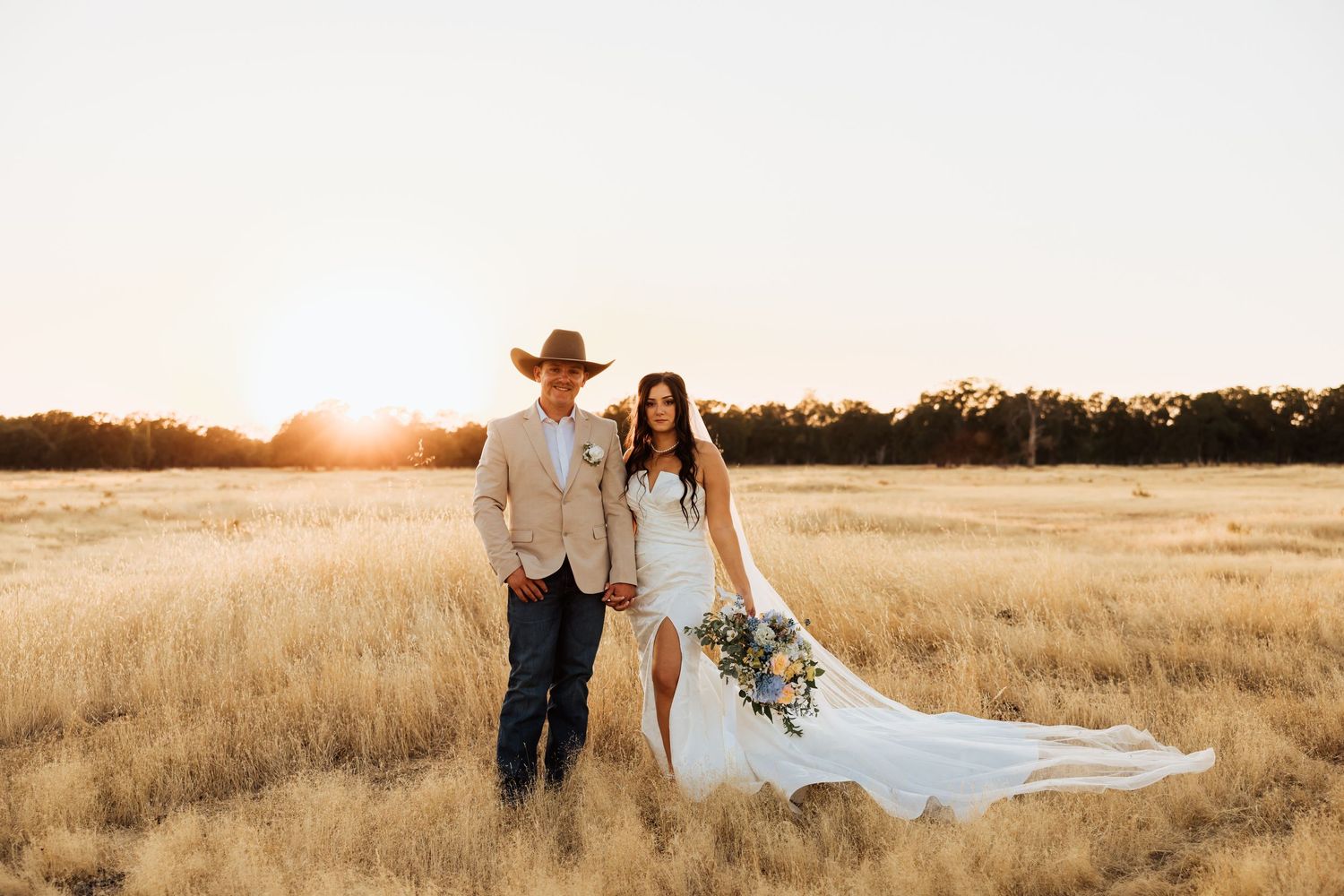 A sunset wedding portrait in a golden field with tall grass and warm lighting.