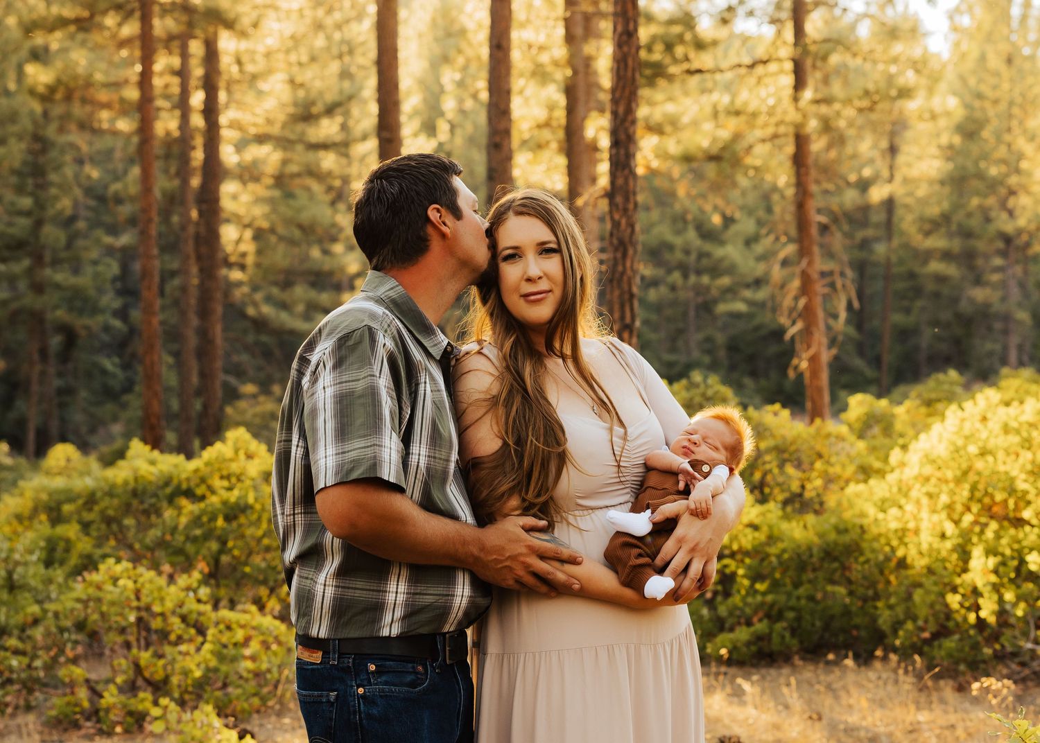 A tender family moment captured in a forest with warm sunset lighting filtering through trees.