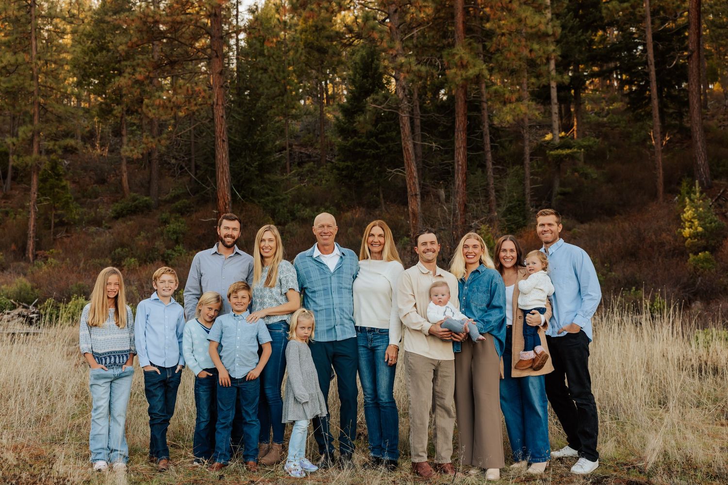 A large family group poses together in coordinated blue and white outfits against a wooded autumn backdrop.