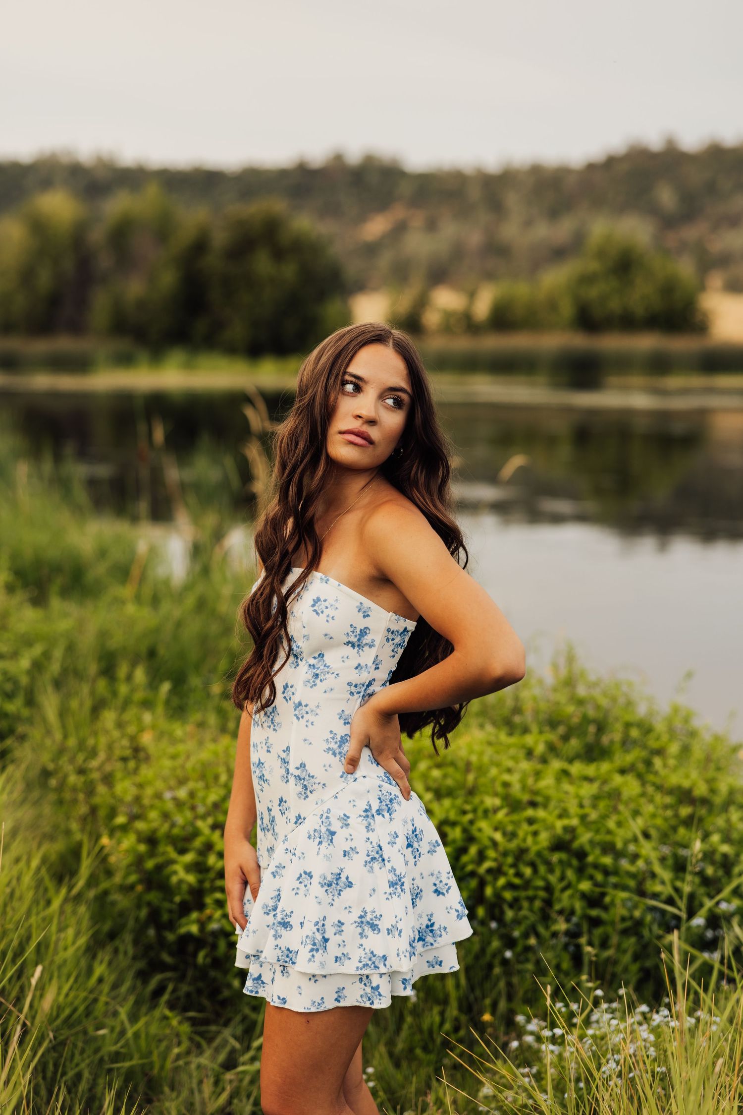 Artistic outdoor photoshoot featuring a blue floral dress against a lakeside landscape.