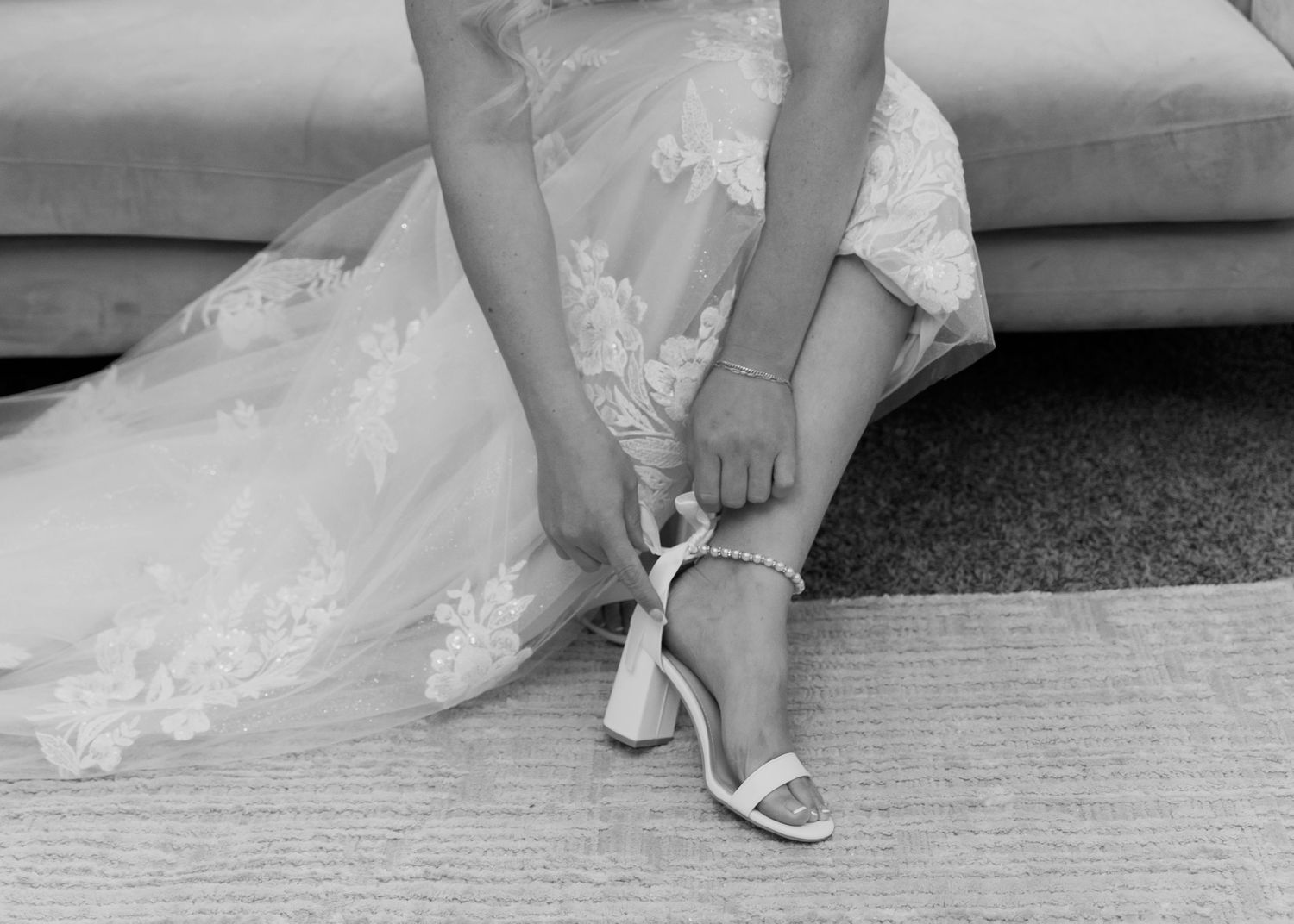 Close-up details of bridal shoes and wedding dress hem on a textured floor.