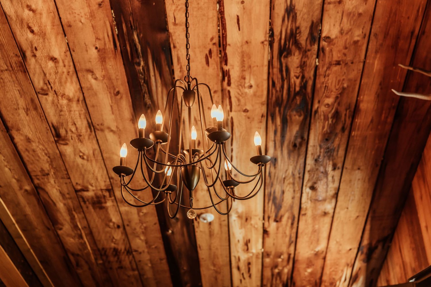 Rustic wooden ceiling with vintage chandelier in warm lighting.