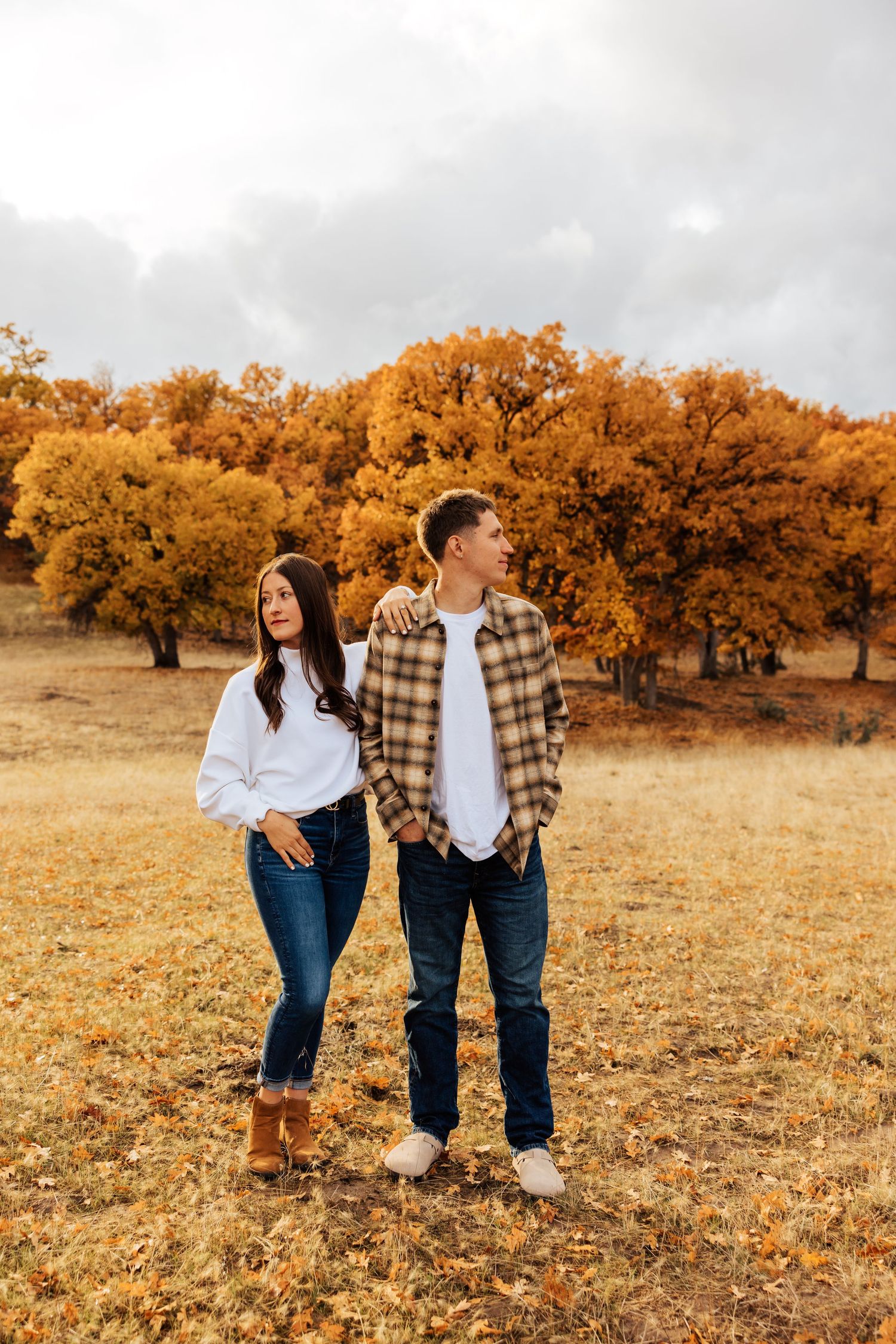 Romantic couple strolling together in a field with vibrant fall foliage behind them.
