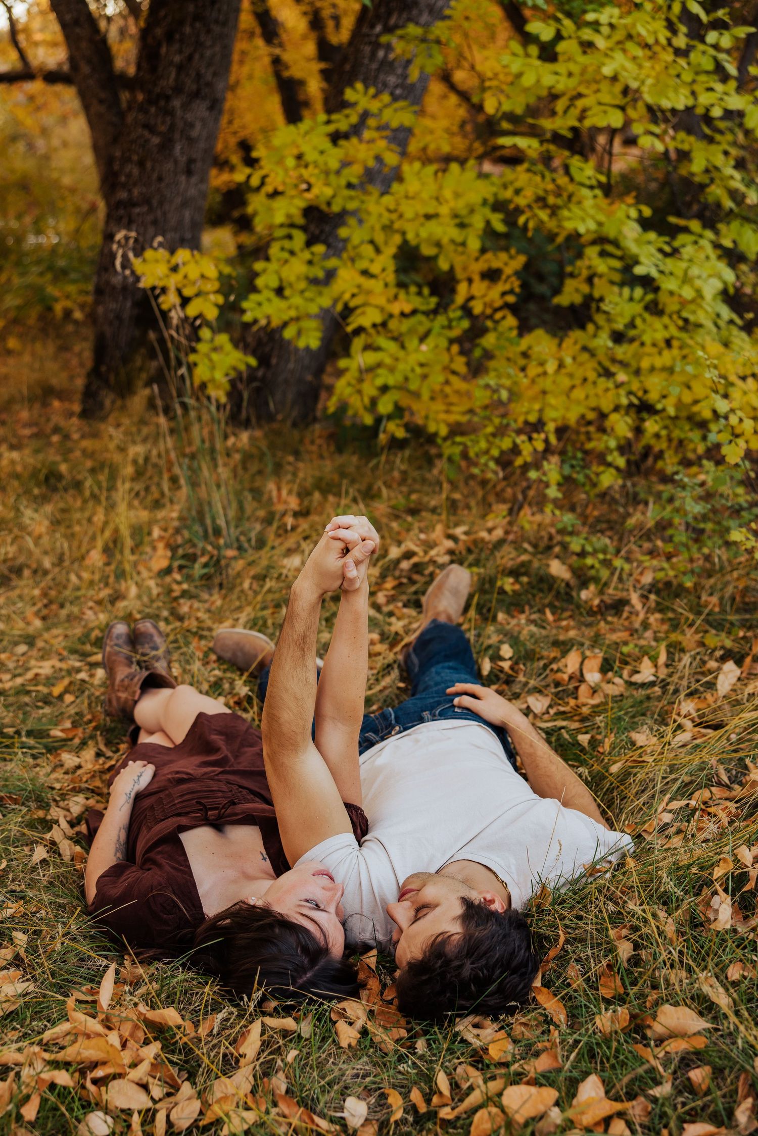 Two people relaxing on fallen leaves under yellow autumn trees.