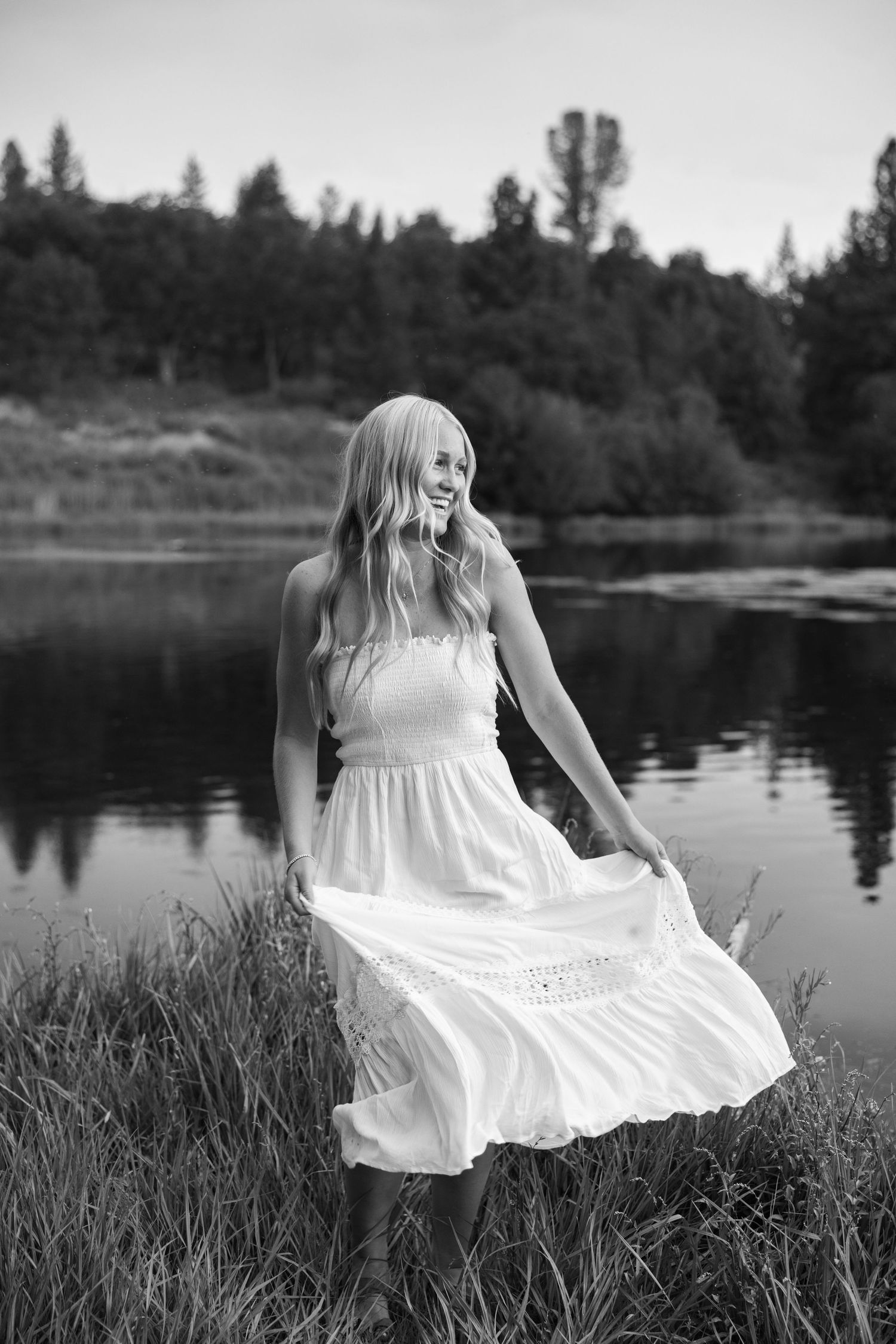 Black and white portrait with flowing white dress by a tranquil lake.