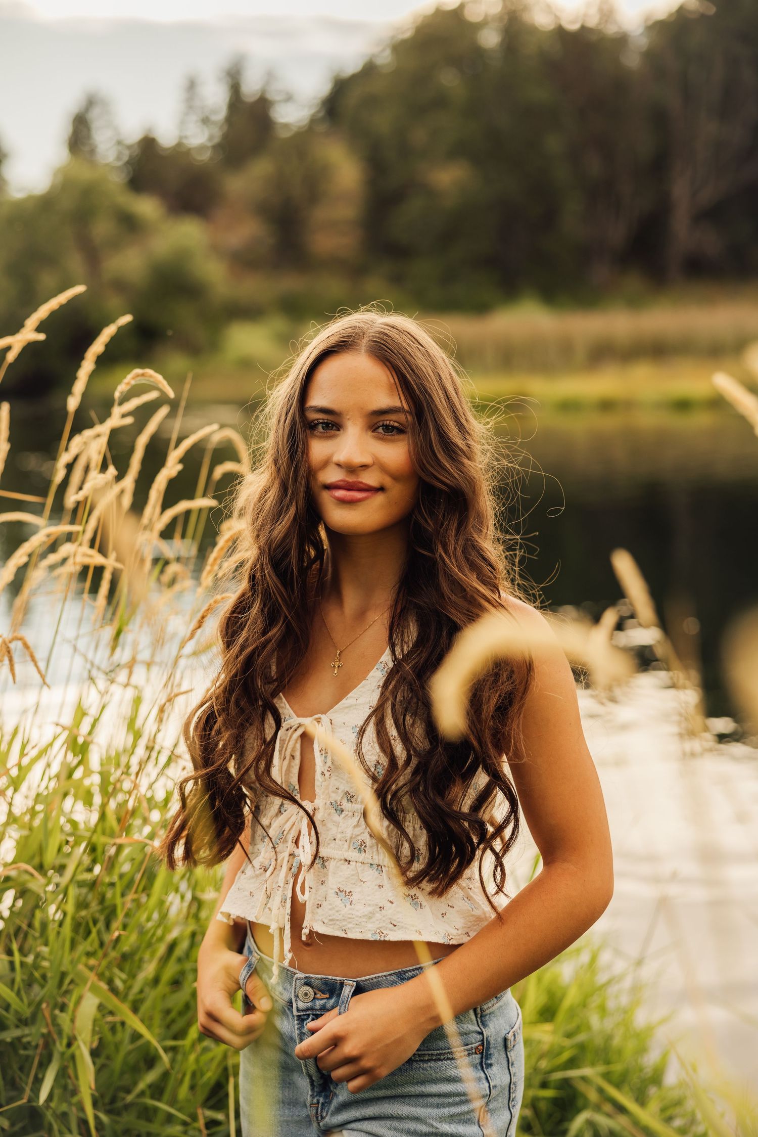 Sunset portrait session among tall grass by a serene lake with golden light.