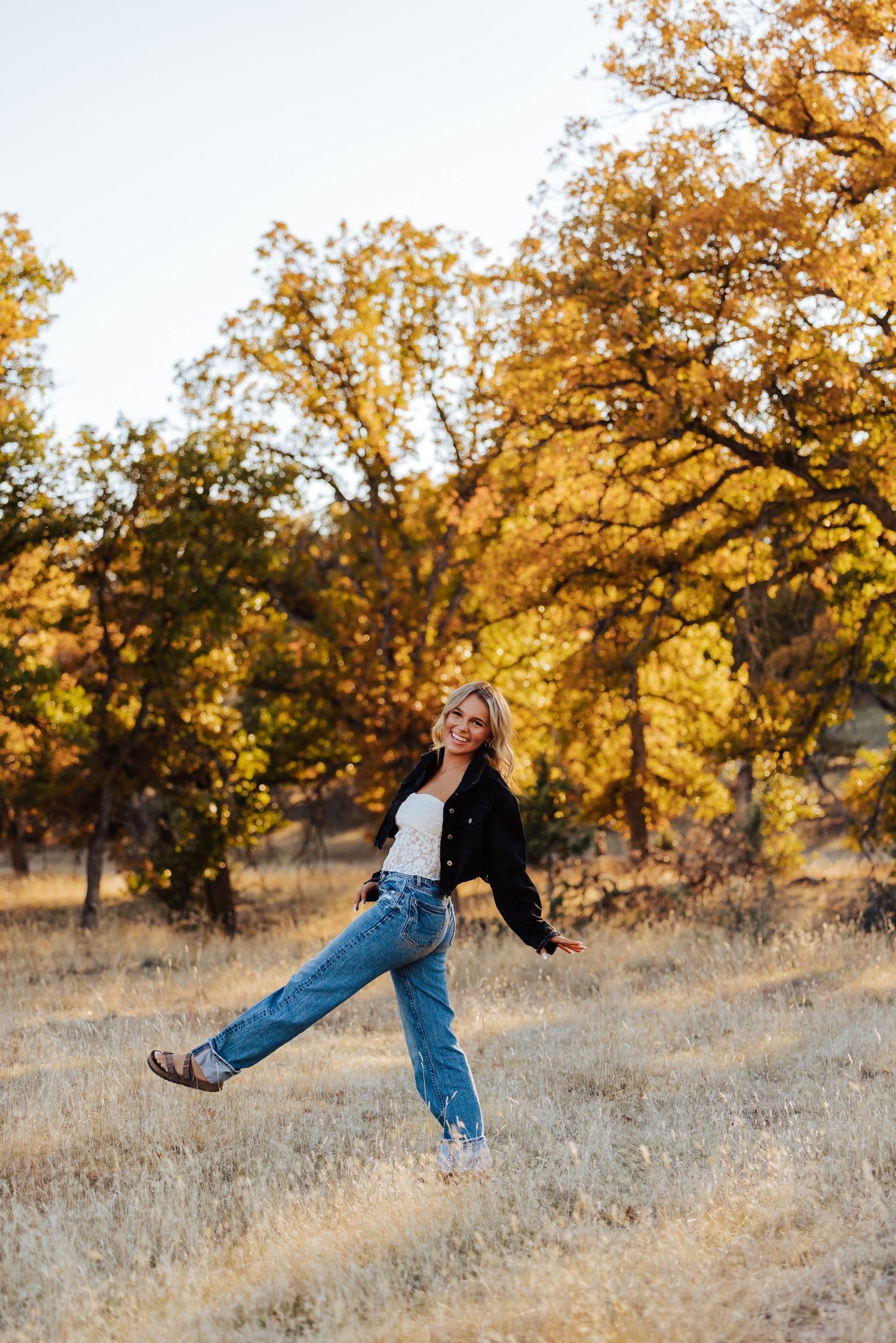 Playful outdoor poses captured against a backdrop of fall trees and golden grass.