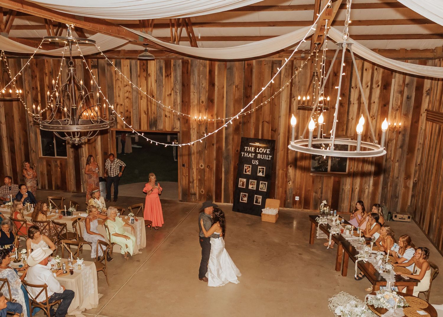 Panoramic view of a barn wedding reception with string lights and white fabric draping the ceiling.
