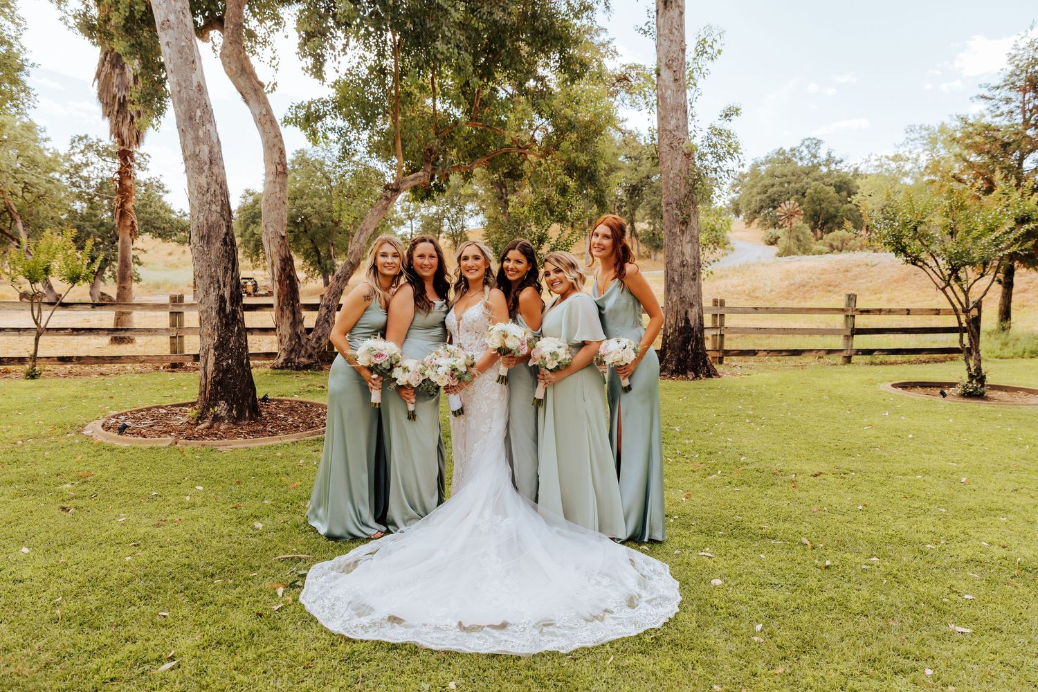 Wedding party in light blue bridesmaid dresses posing on grassy lawn.