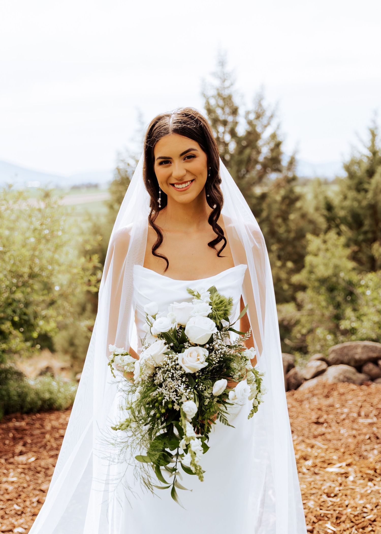 A bride holds a beautiful white and green wedding bouquet against a natural backdrop.