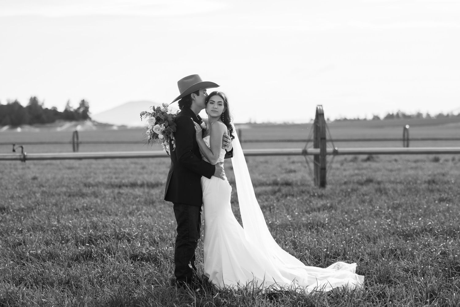 Wedding couple embracing in a vast field with mountains in the background.