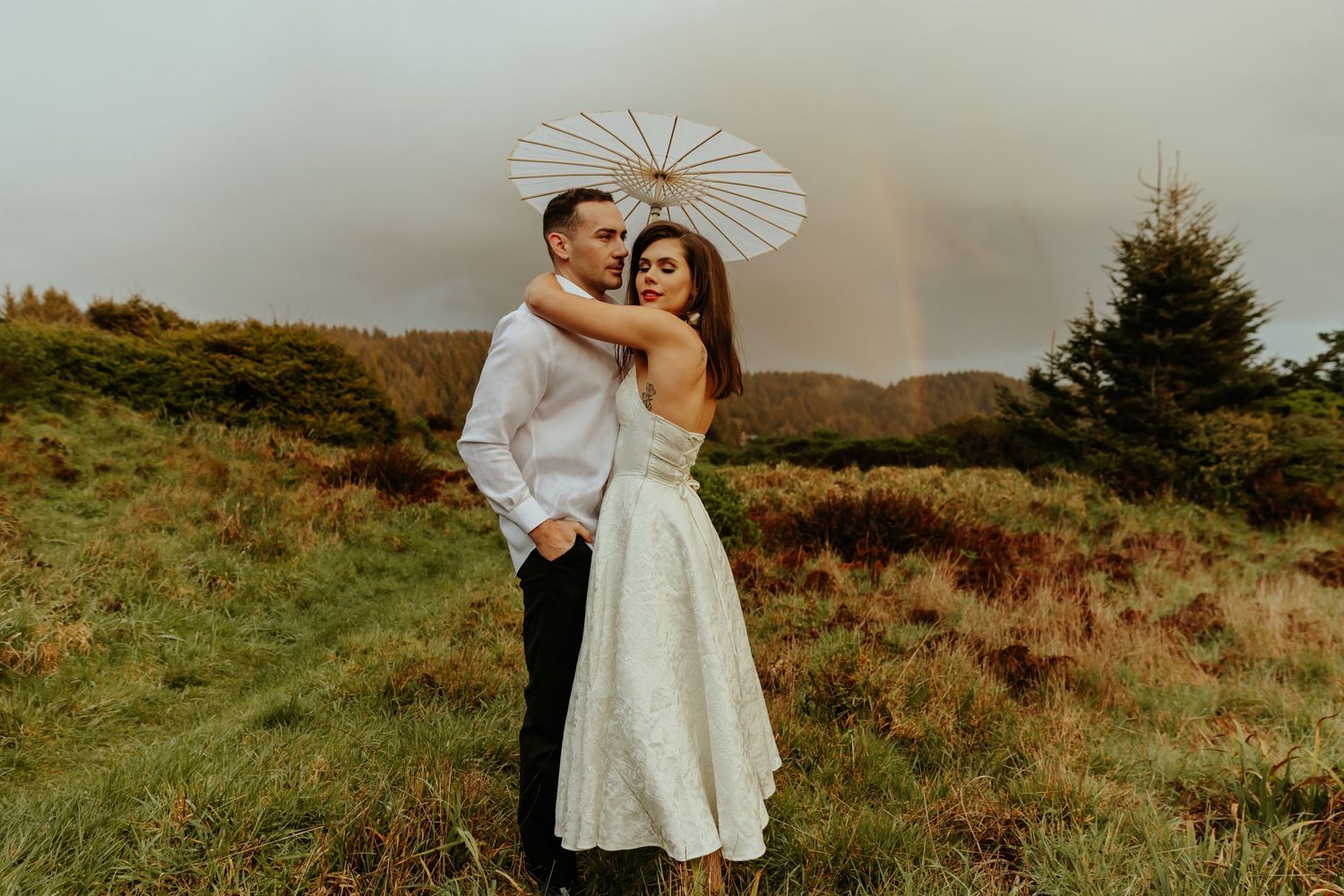 A couple shares tender moments on a coastal hillside with a decorative white parasol.