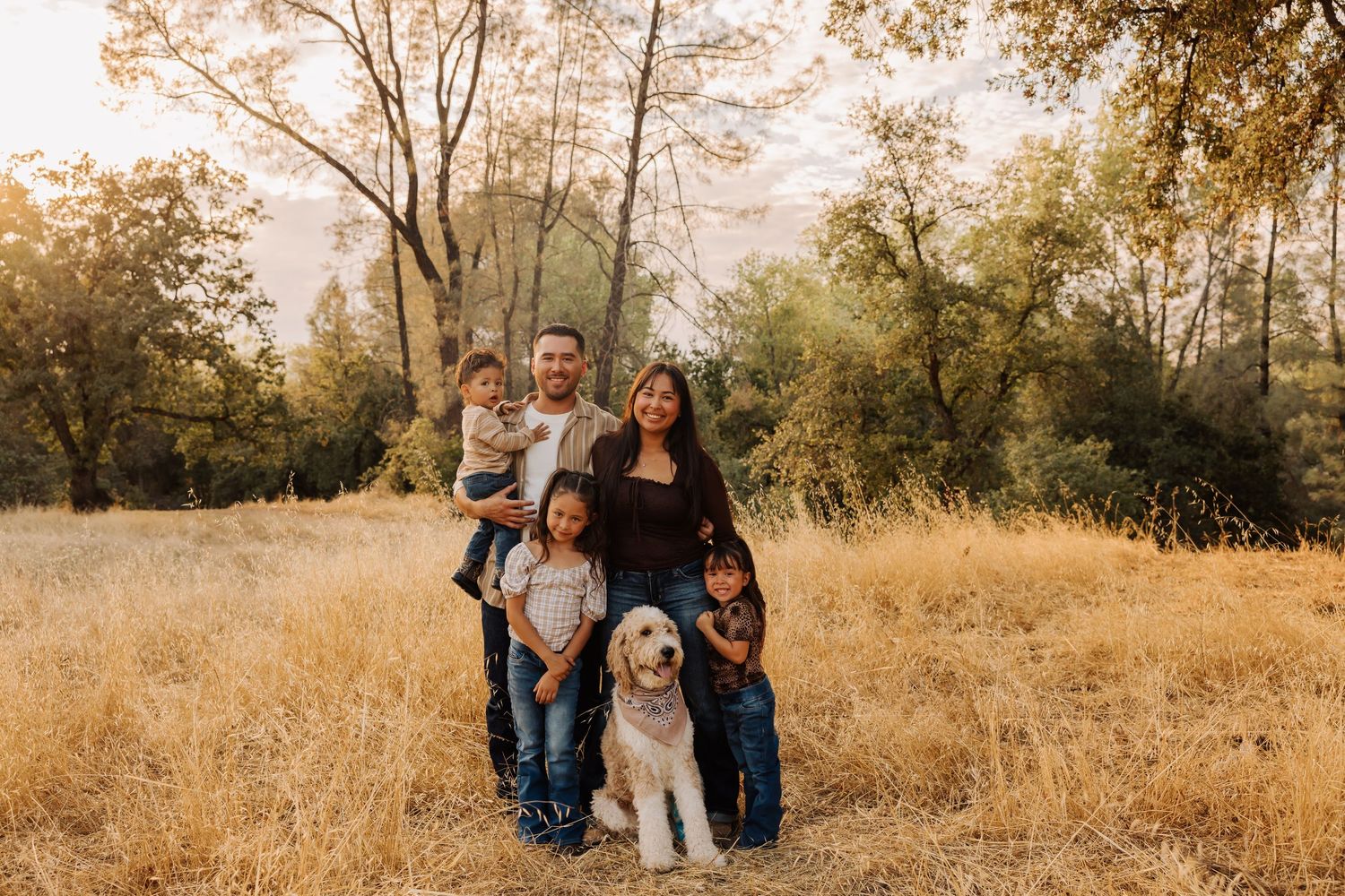 Family with dog poses for outdoor portrait in autumn field at sunset.