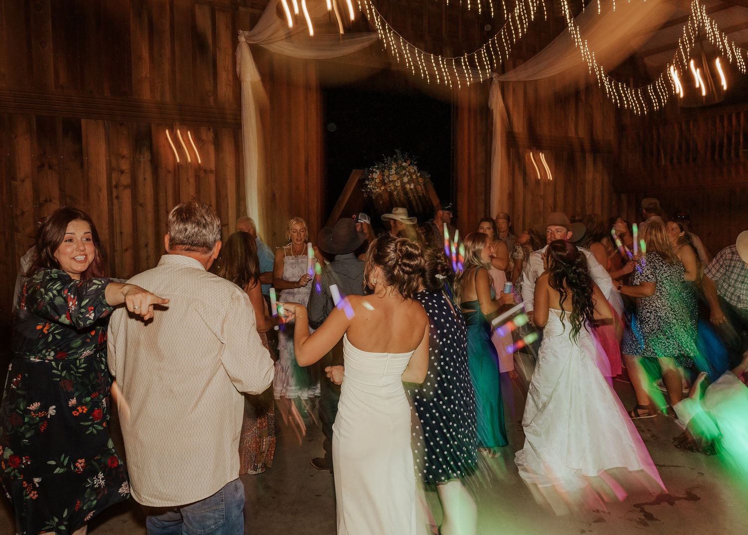 Wedding guests dancing and celebrating on a rustic wooden dance floor at a reception.