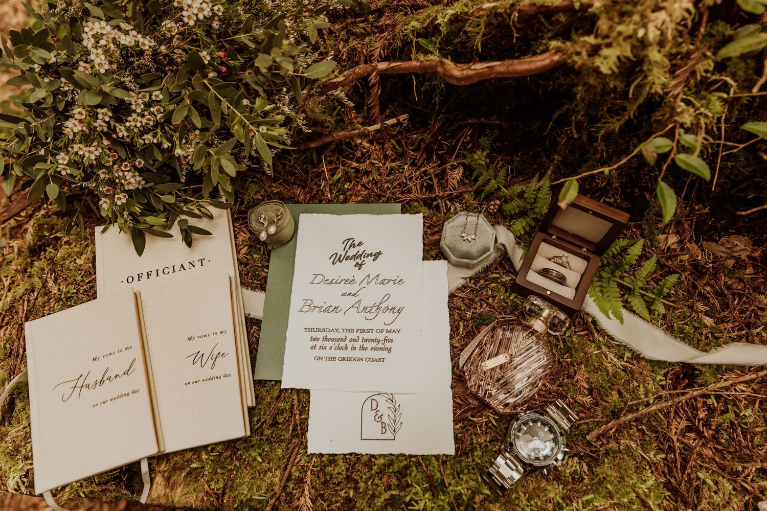 Wedding invitation suite and jewelry arranged on forest floor with natural elements.