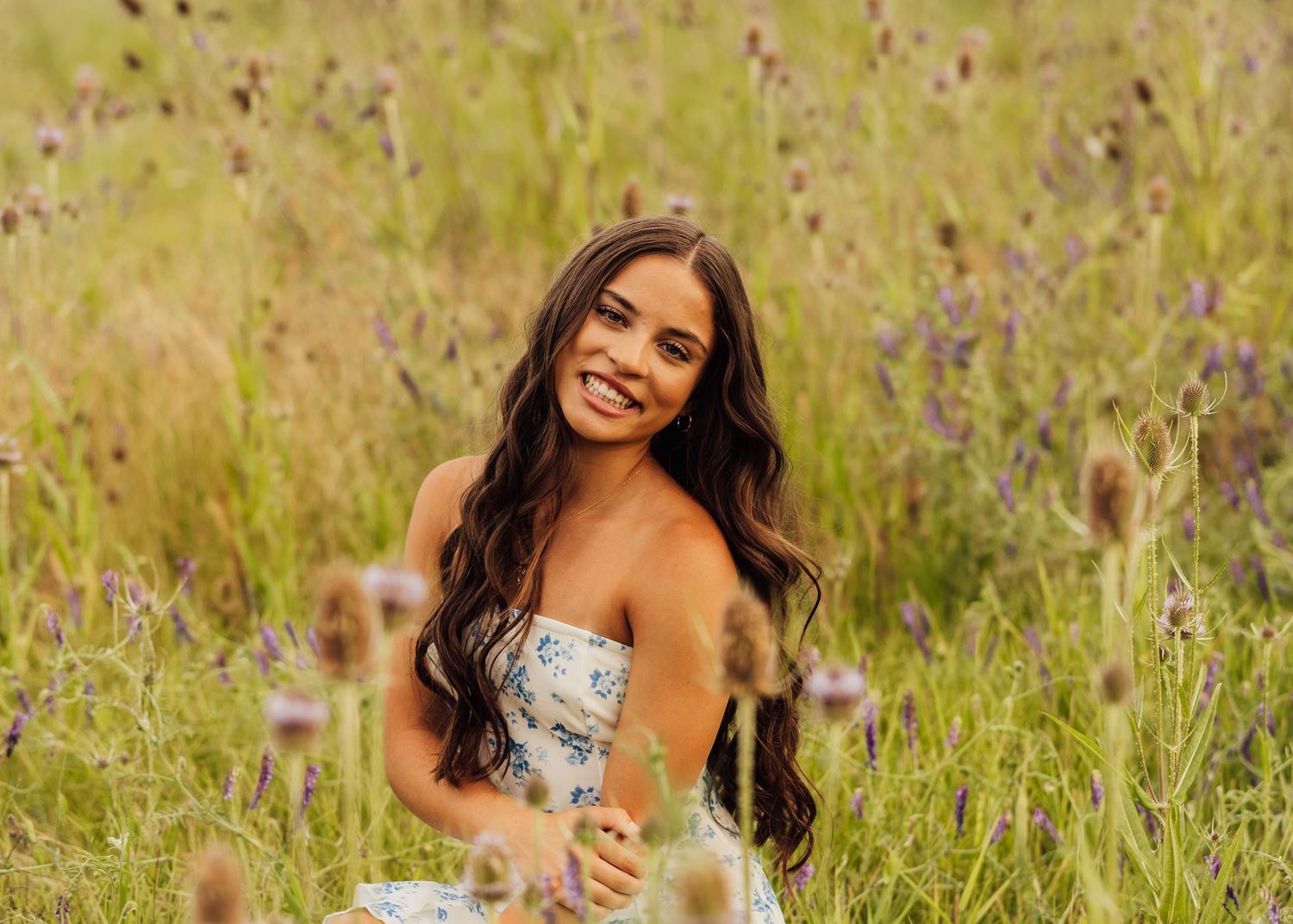 A person in a white dress poses gracefully in a field of purple wildflowers during golden hour.