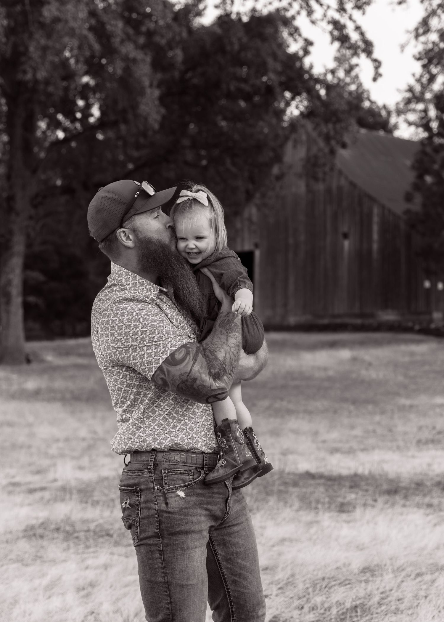 Black and white family moments captured in a field with rustic barn backdrop.