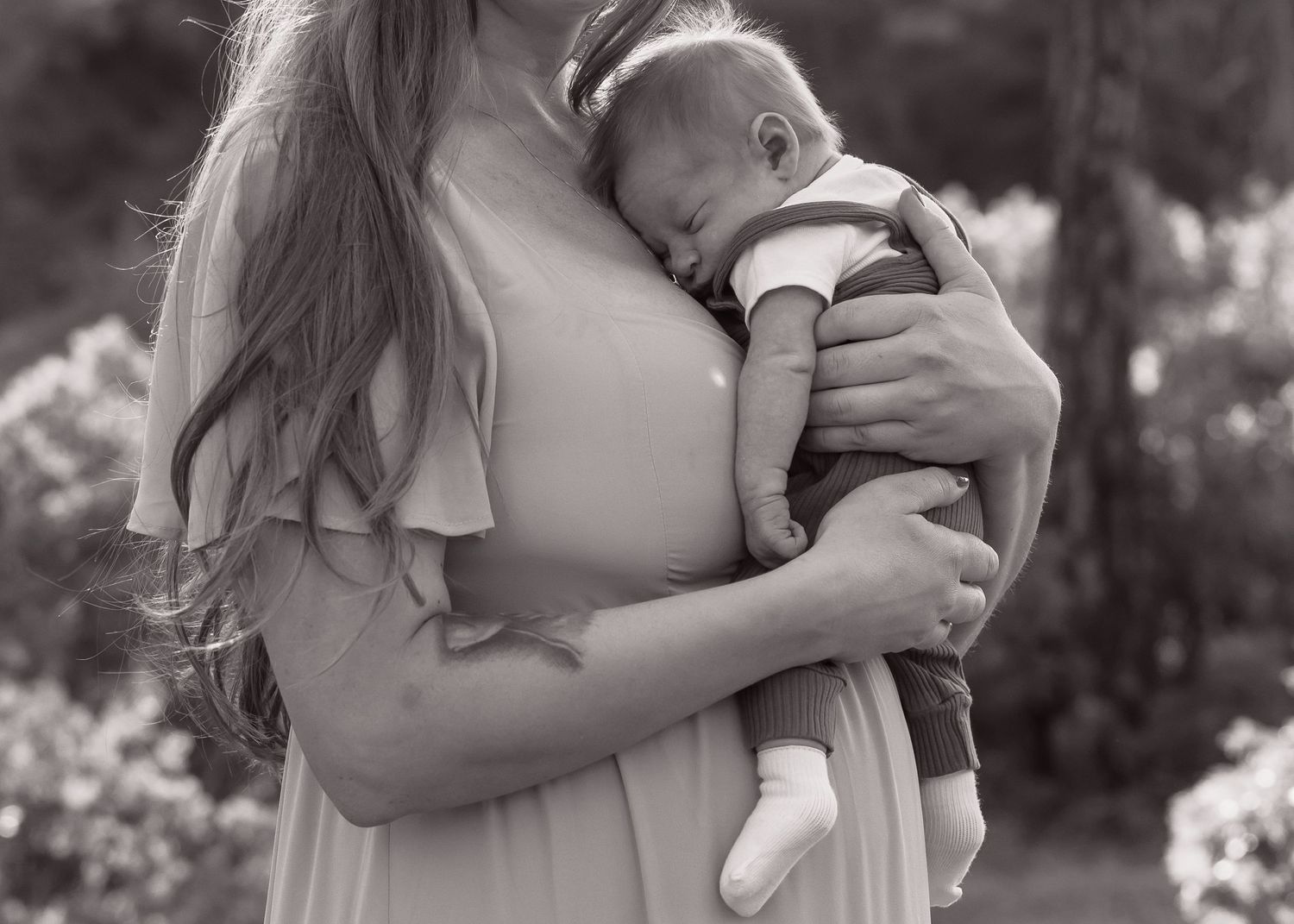 Close-up black and white photo of a mother holding a sleeping infant in a flowing dress.
