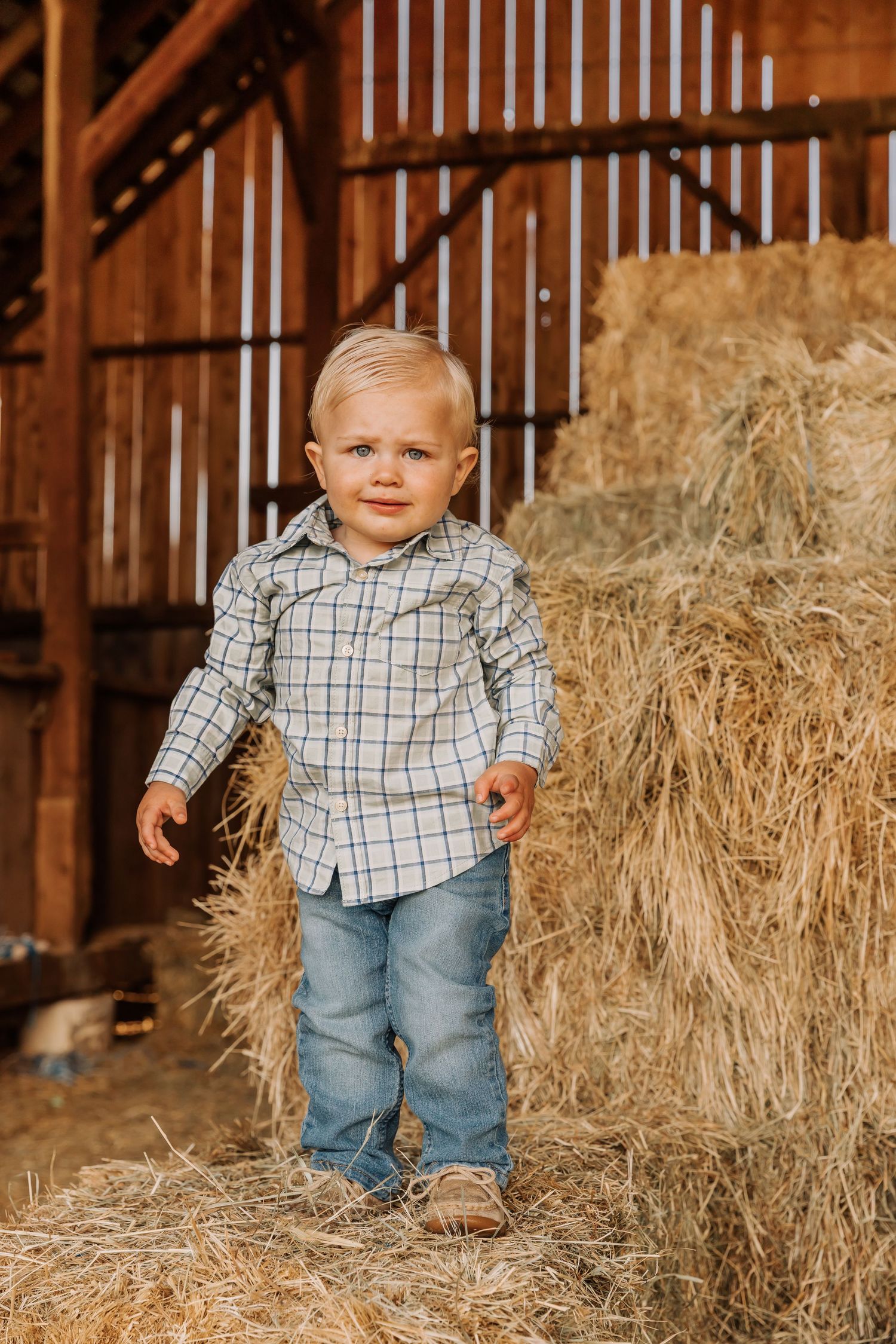 A toddler explores hay bales inside a rustic wooden barn.