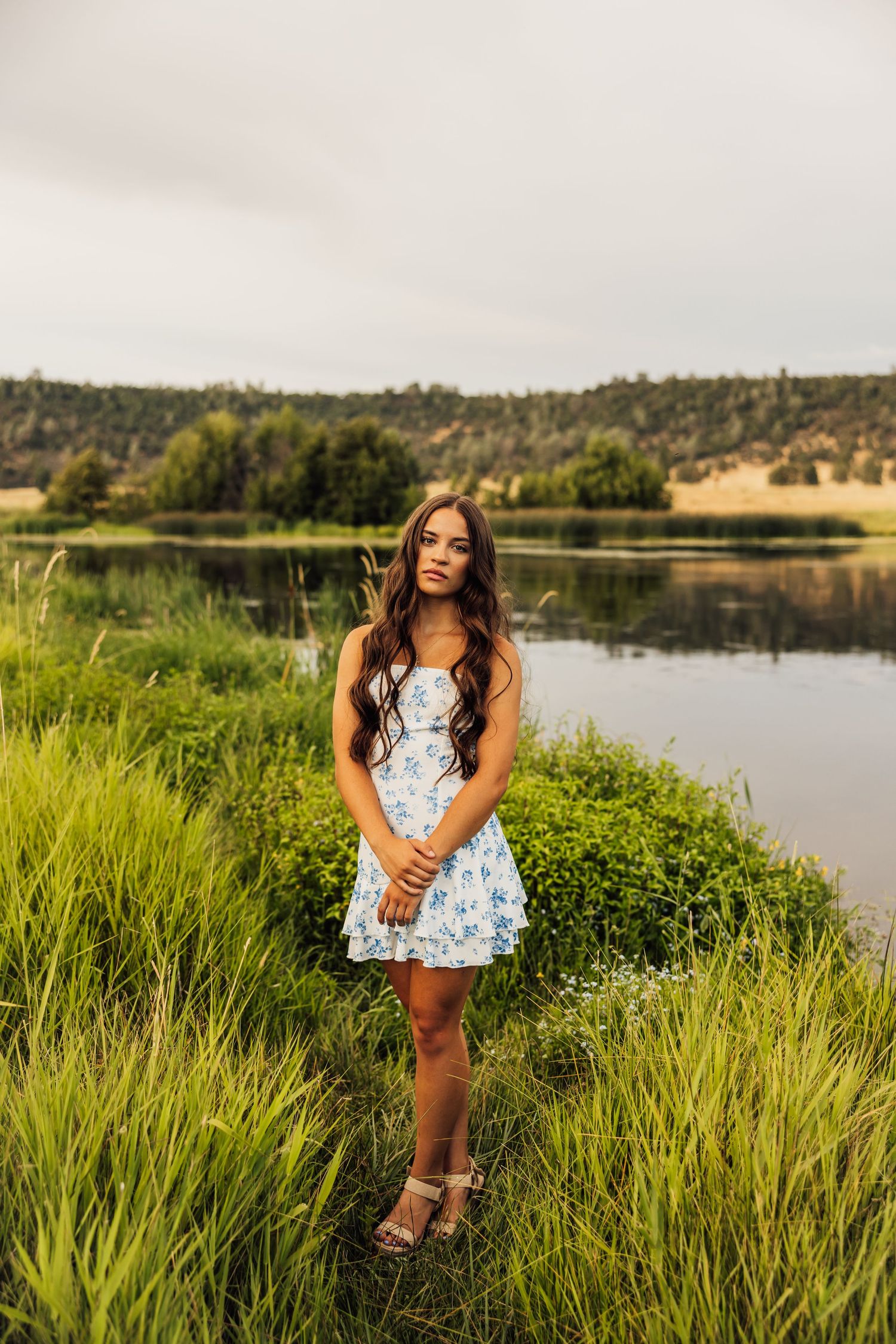Summer portrait session by a tranquil lake with tall green grasses in the foreground.