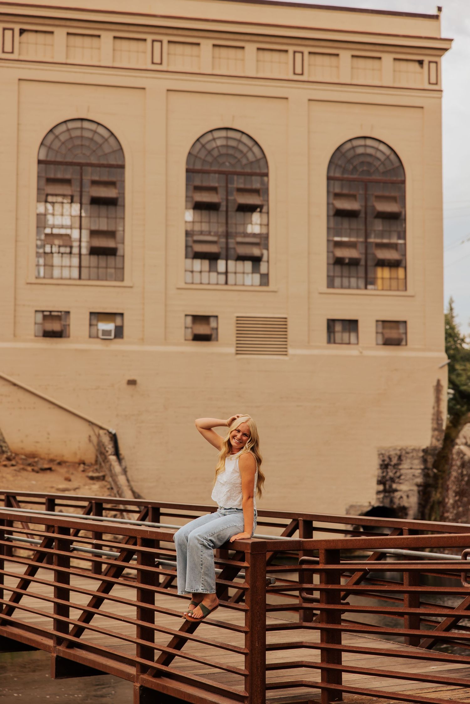 Artistic portrait against vintage building with arched windows and wooden bridge railing.
