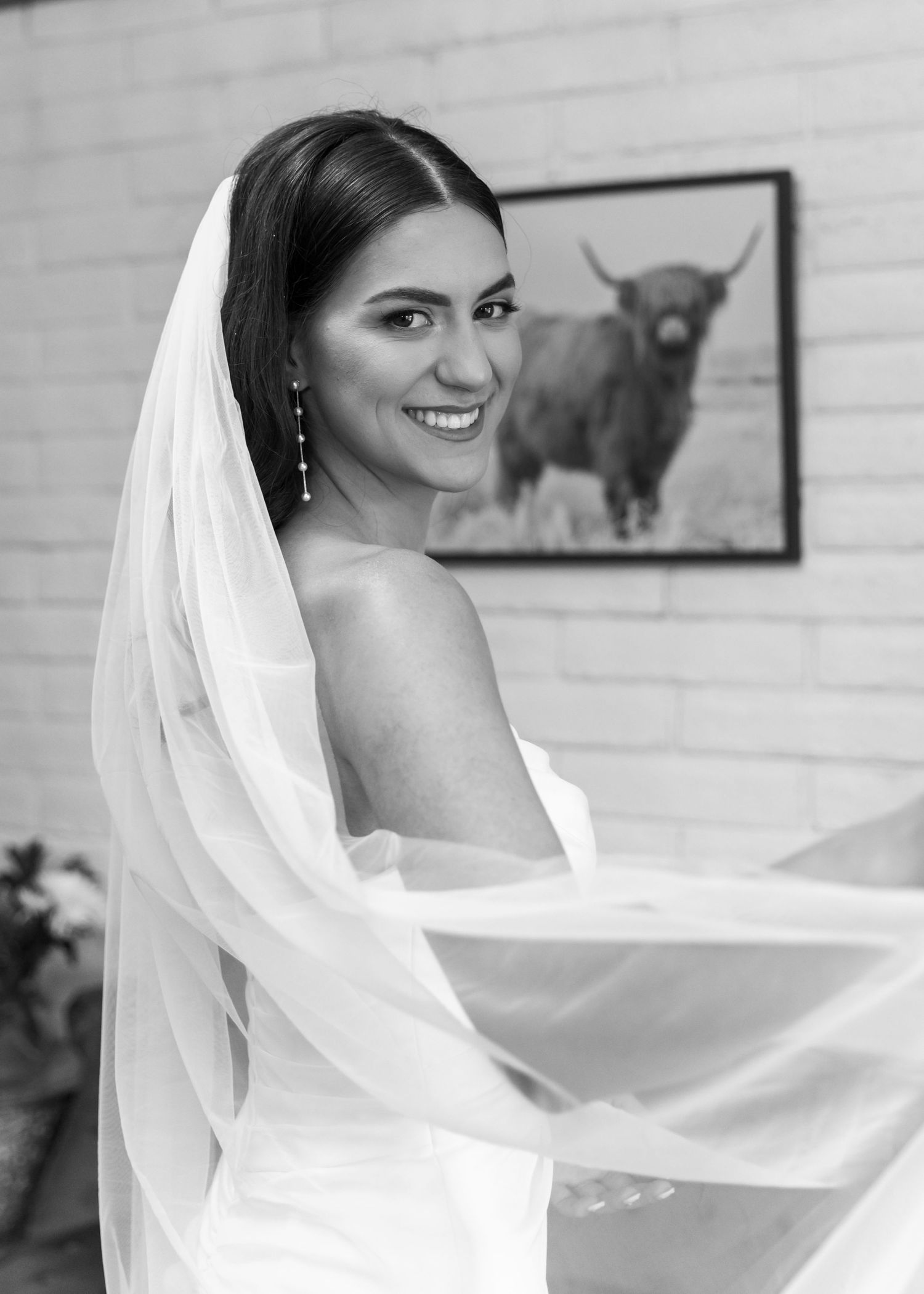 Bride in white dress twirling and showing off her wedding veil in a rustic room.