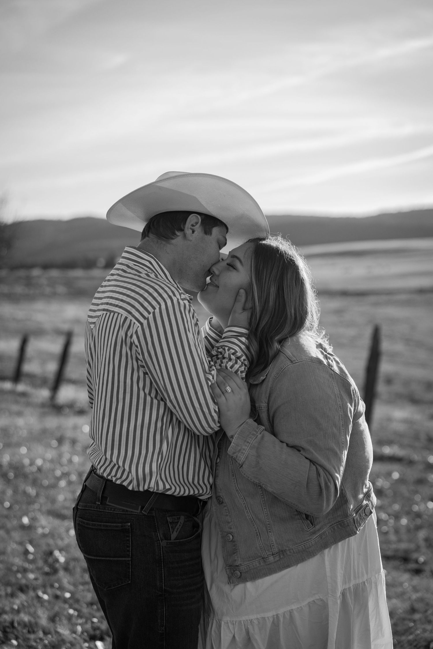 A black and white romantic moment captured in a rural field setting.