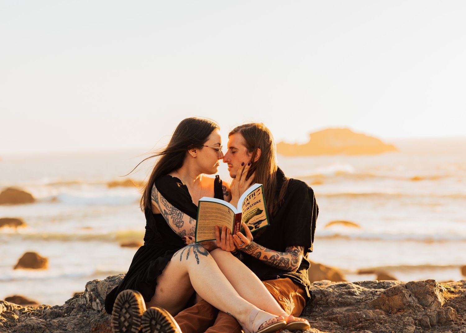 A couple shares an intimate moment on rocky beach during golden hour.
