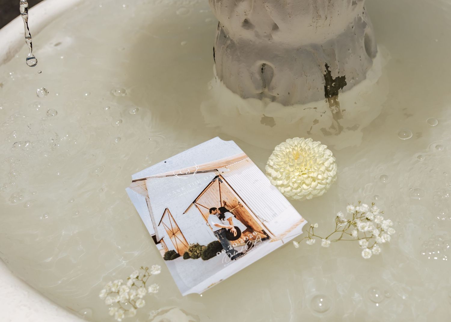 A wedding photo card and white flower floating in a white bathtub filled with water.