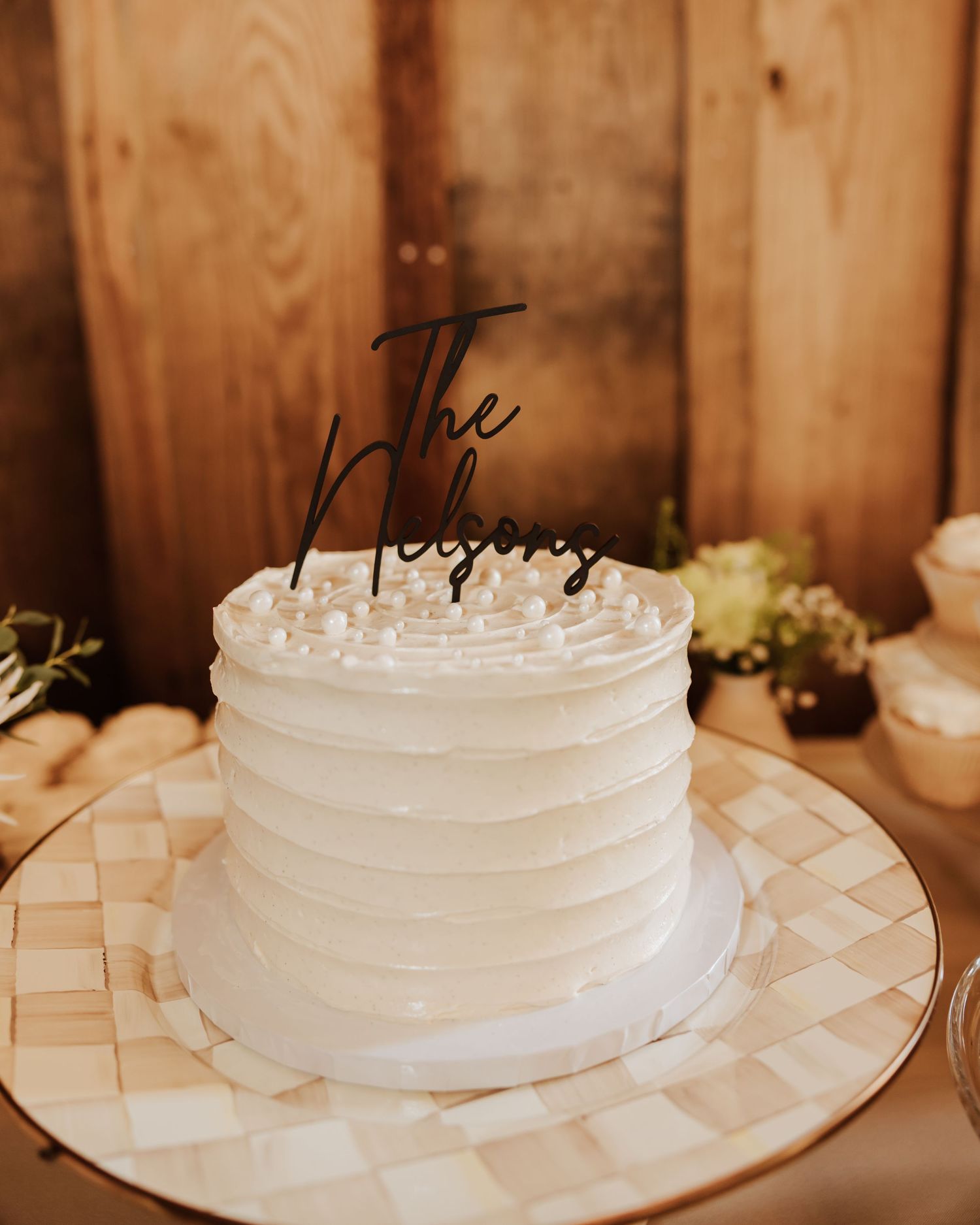 Simple white wedding cake displayed on a checkered plate against rustic wooden backdrop.
