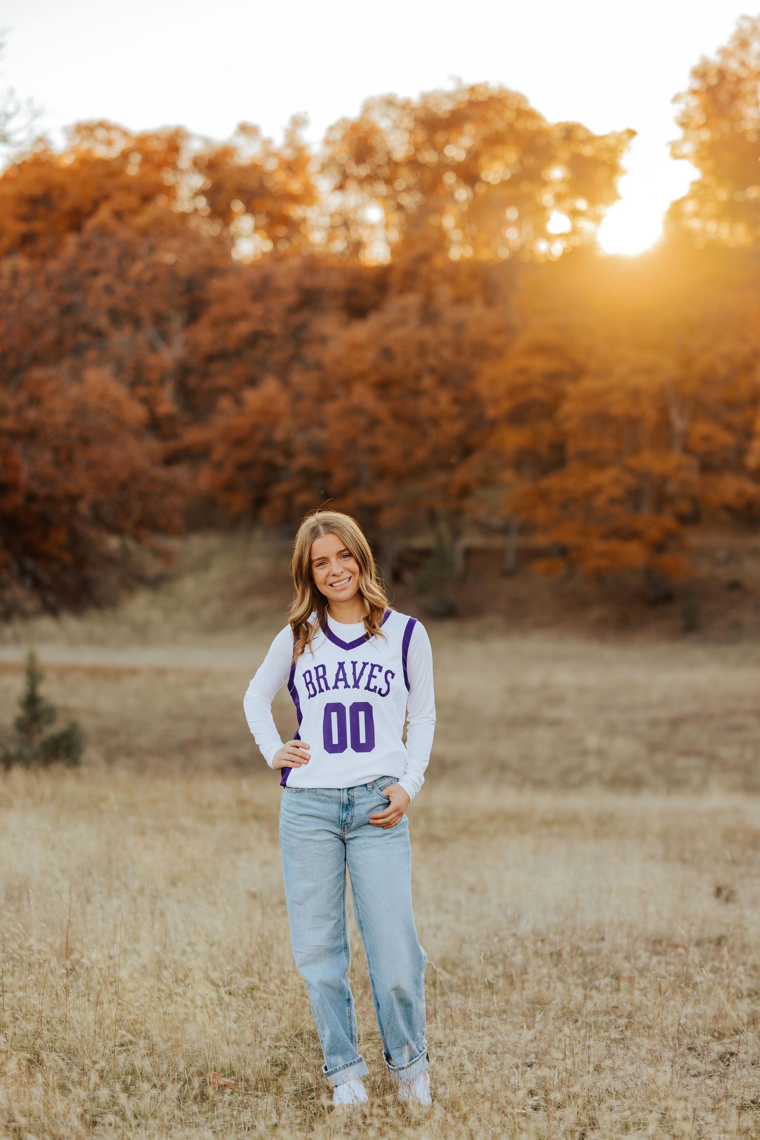 Athletic senior photos featuring sports jerseys in a sun-drenched autumn field.