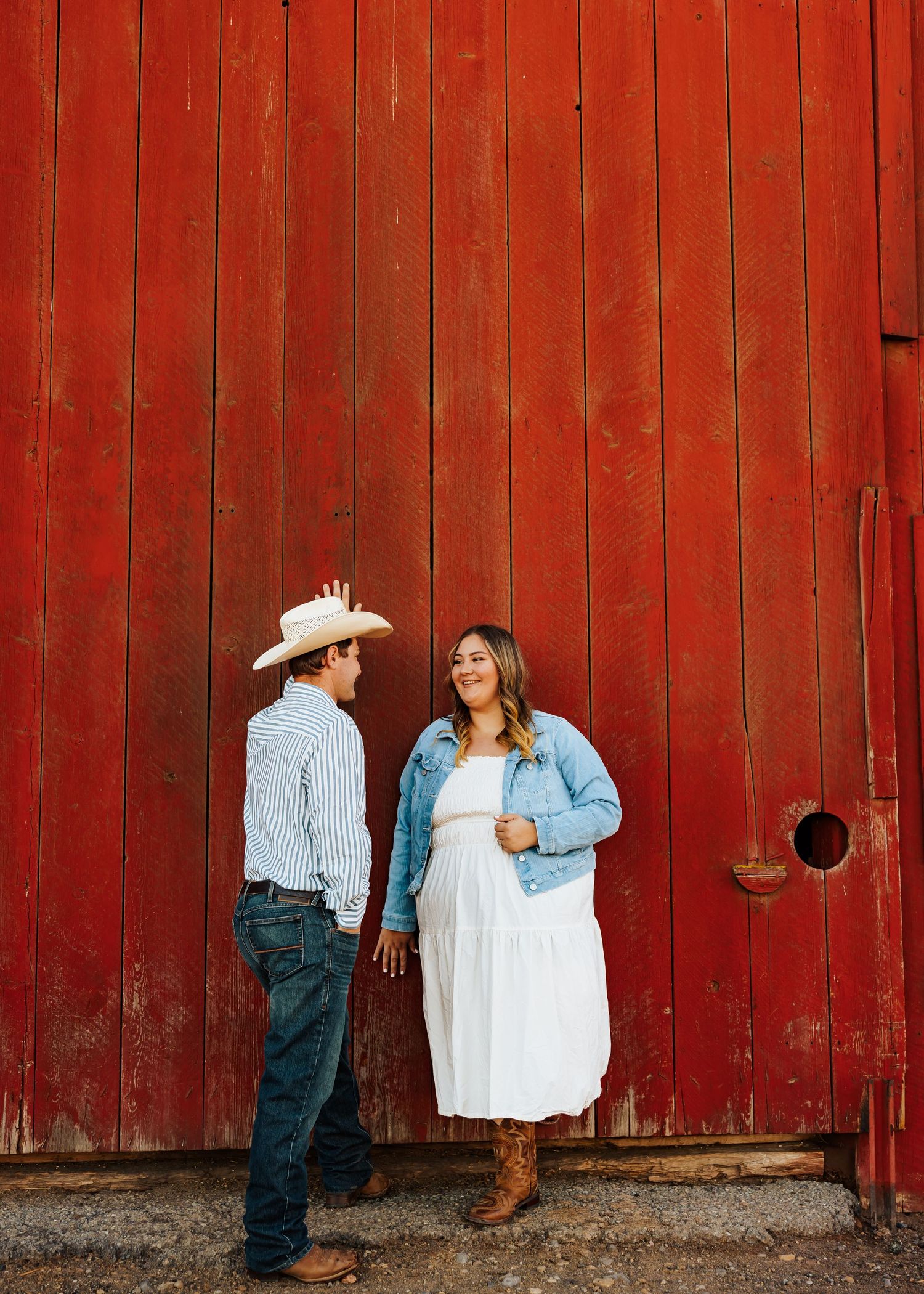A couple shares an intimate moment against a weathered red barn wall.