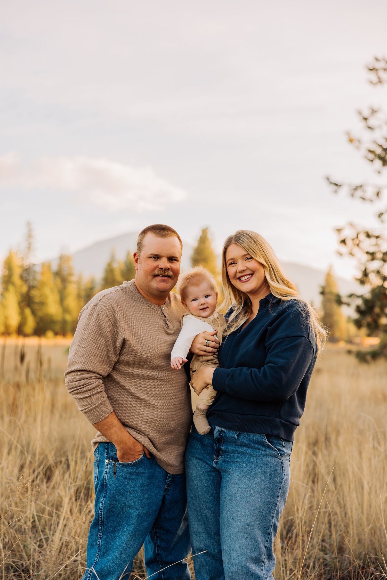 Joyful family portrait session in tall grass with mountain scenery.