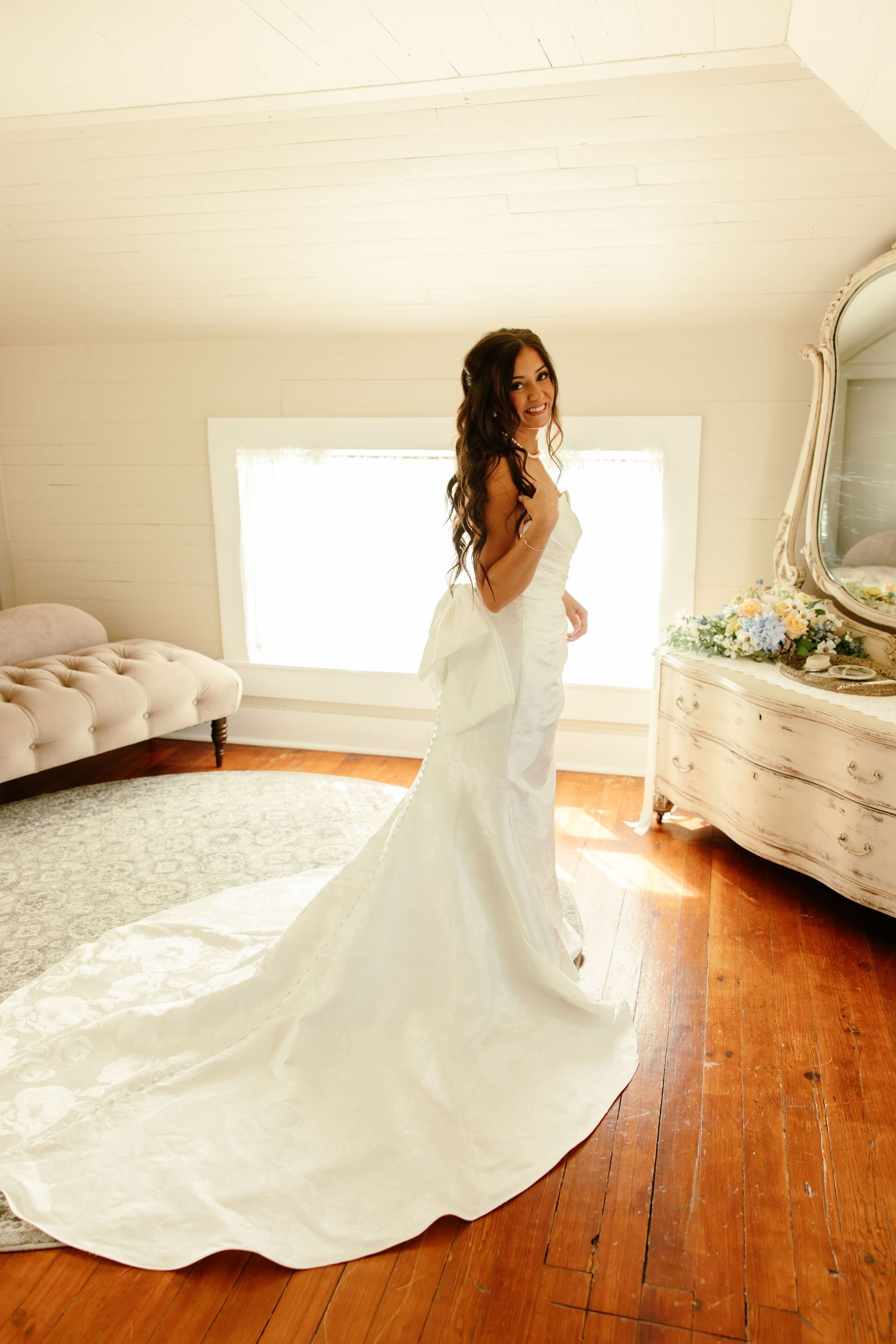 White wedding dress with flowing train twirls gracefully across hardwood floors in sunlit room.