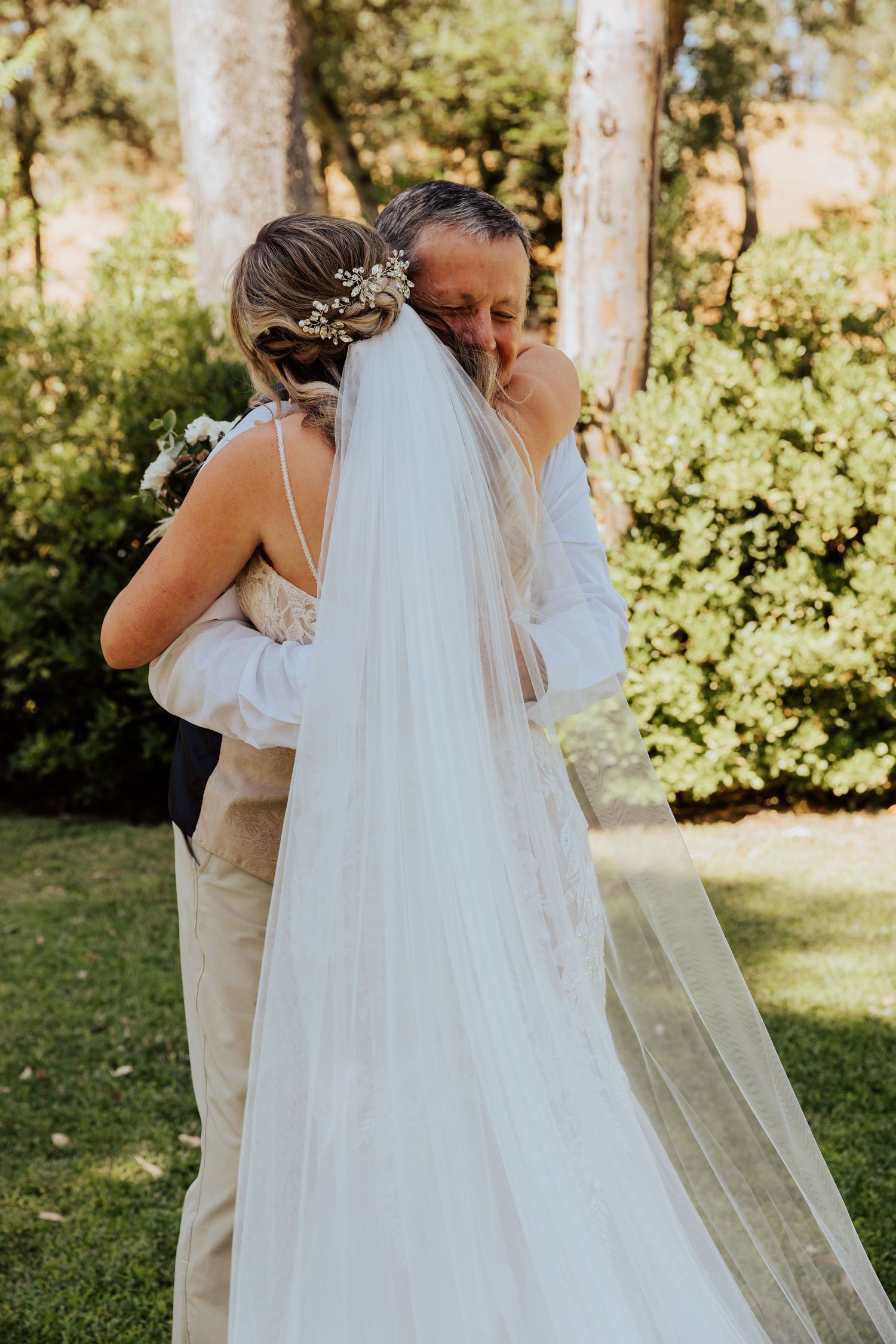 Wedding couple embracing in sunlit garden setting with flowing white veil.