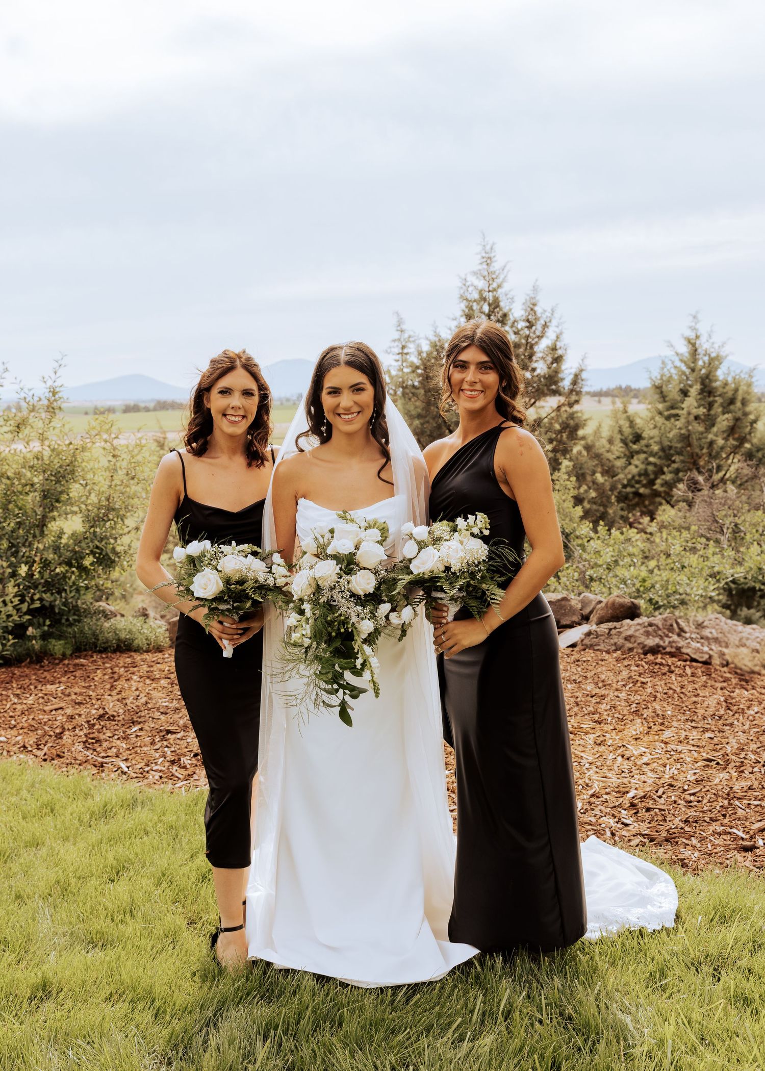 Wedding party in black and white dresses posing with bouquets outdoors.
