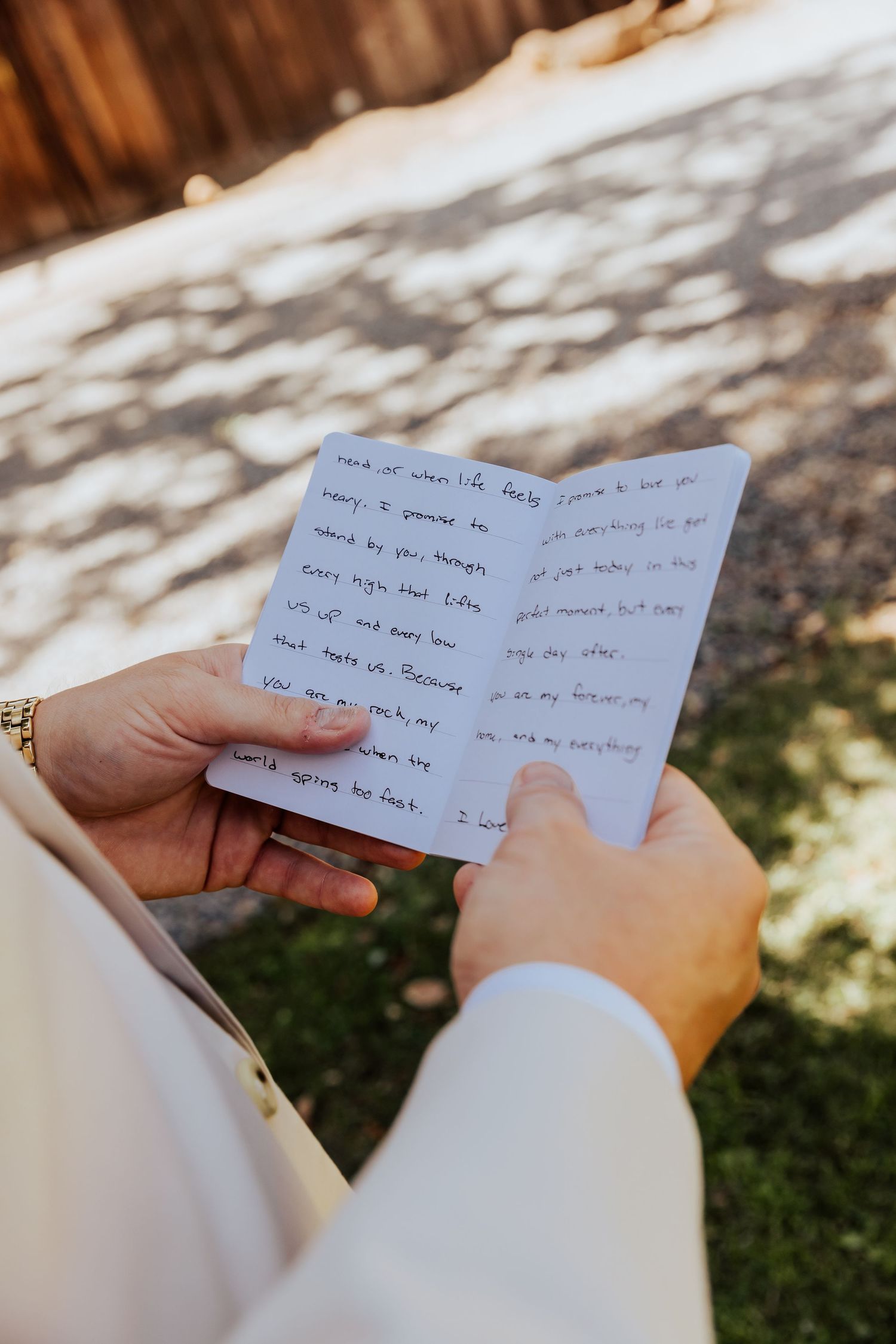 Hands holding handwritten wedding vows on paper in outdoor lighting.