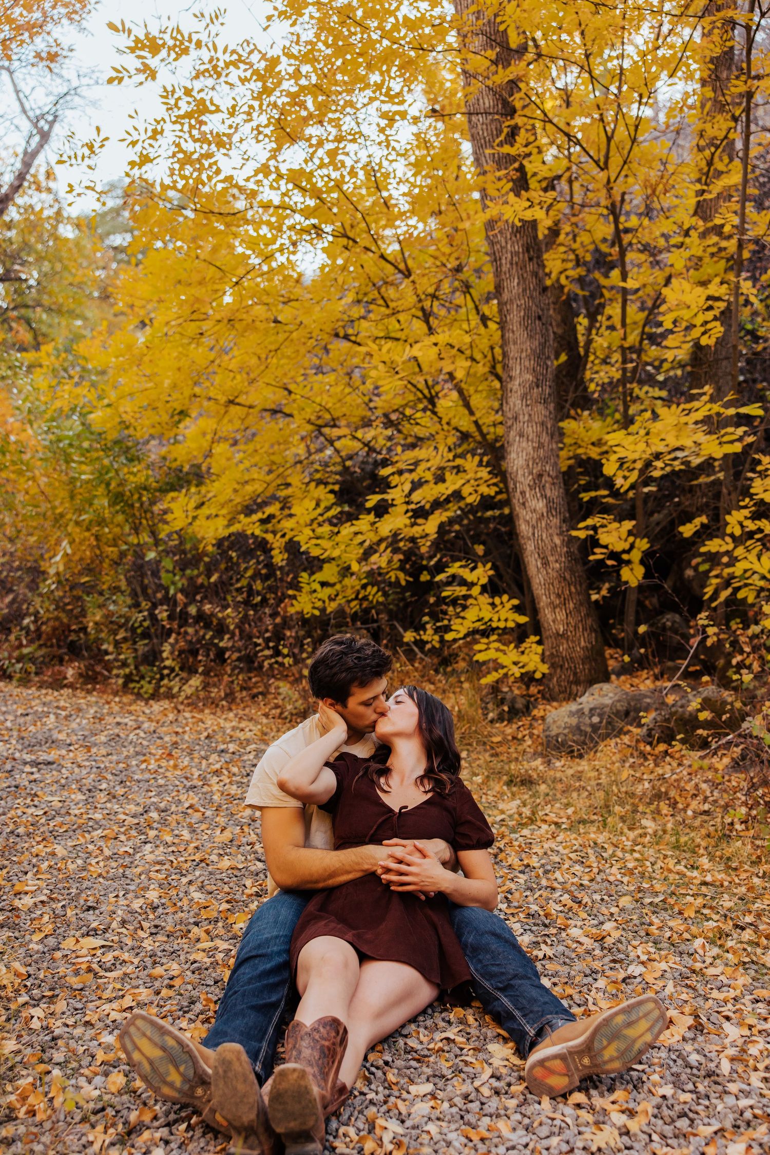 Romantic couple sharing intimate moments on autumn leaves in a golden forest setting.