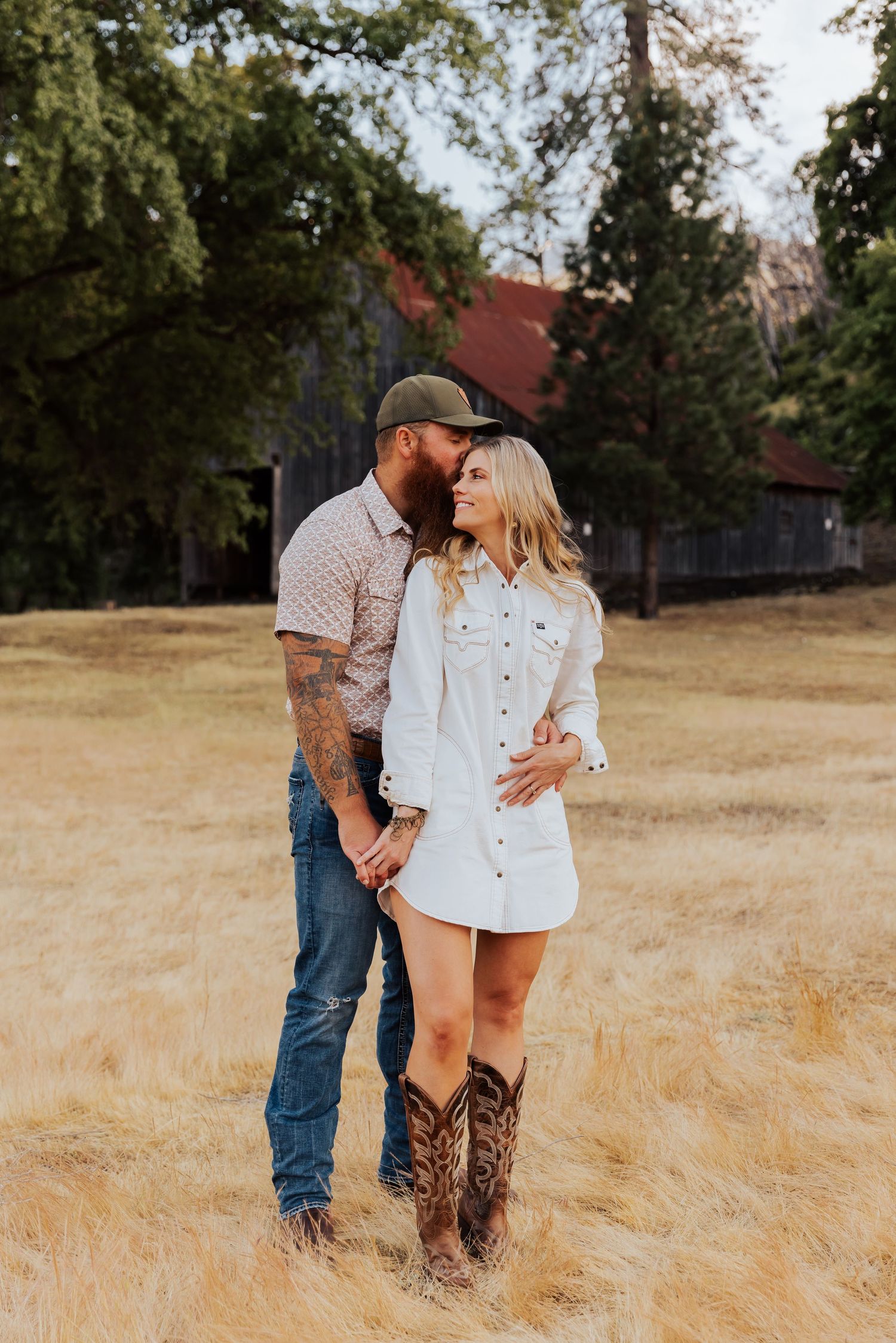 Intimate couple's photoshoot in a rustic setting with golden grass and wooden barn.