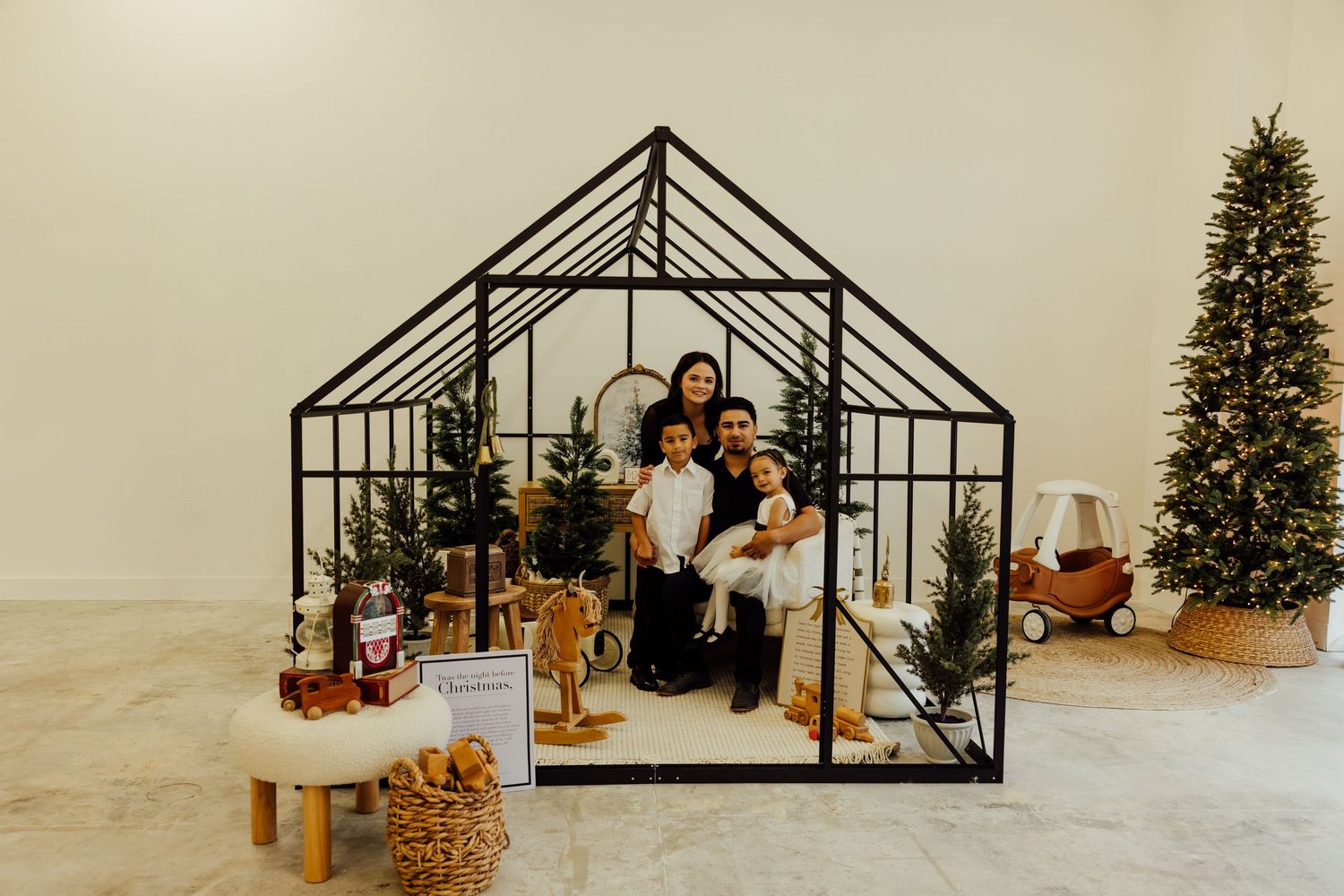 A black metal greenhouse frame silhouette displayed with holiday decorations against a white background.