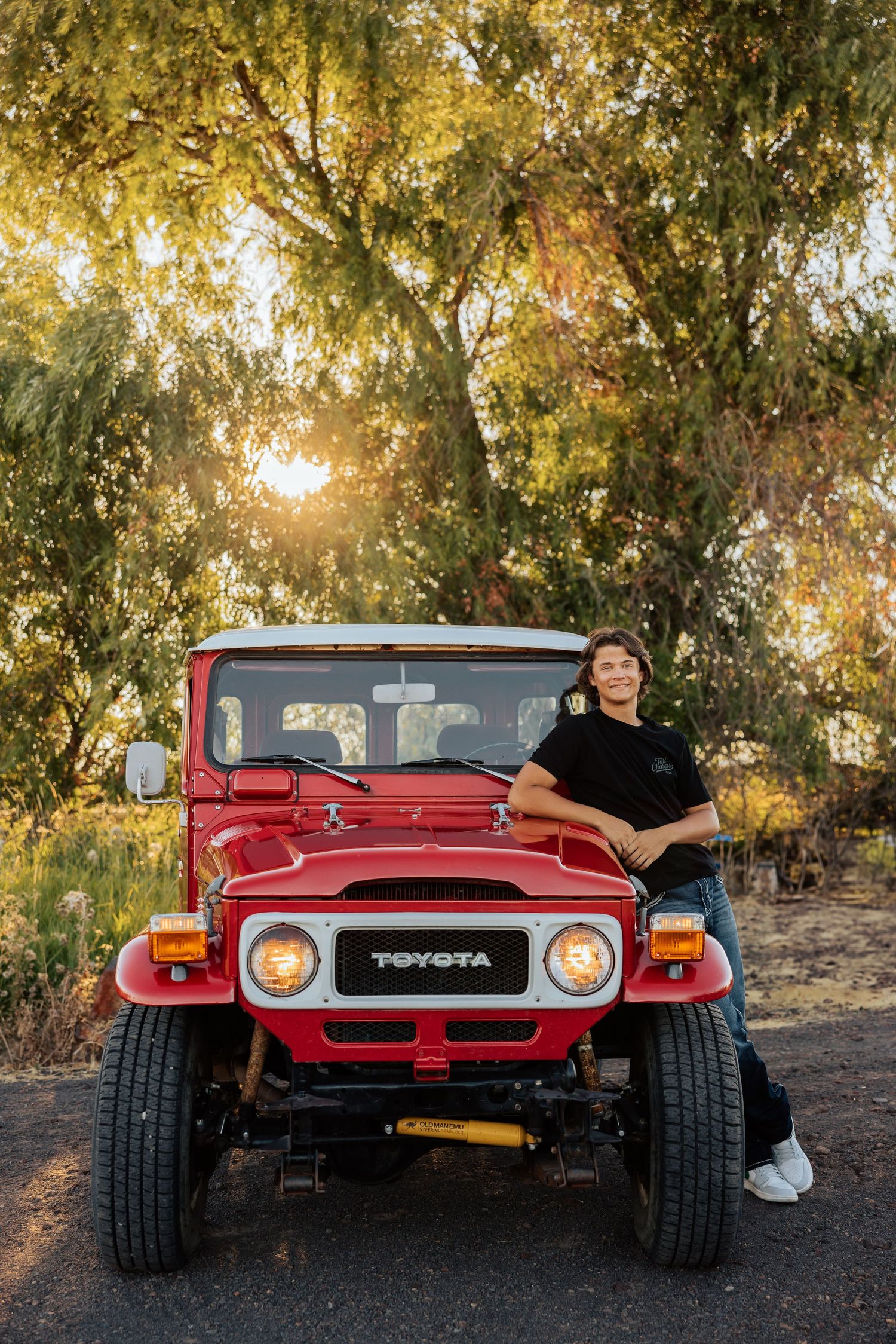 Classic red Toyota Land Cruiser parked among trees during golden hour.