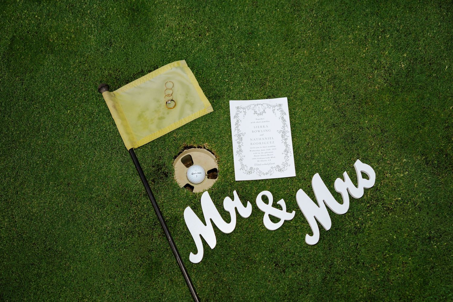 Golf-themed wedding decor with Mr & Mrs sign, golf ball, yellow flag, and invitation on green grass.