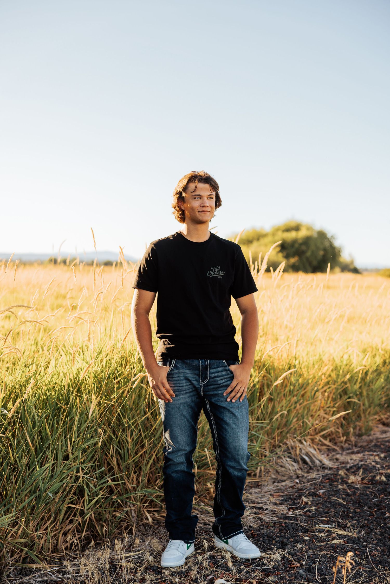 Someone stands in a golden field during sunset wearing jeans and a black t-shirt.