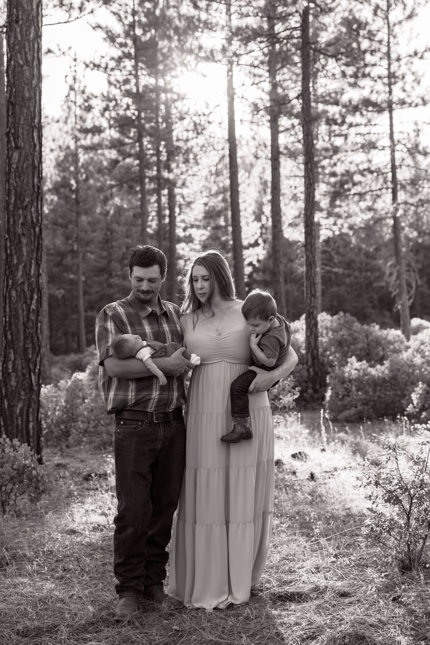 Black and white family portrait in a forest setting with tall pine trees in the background.