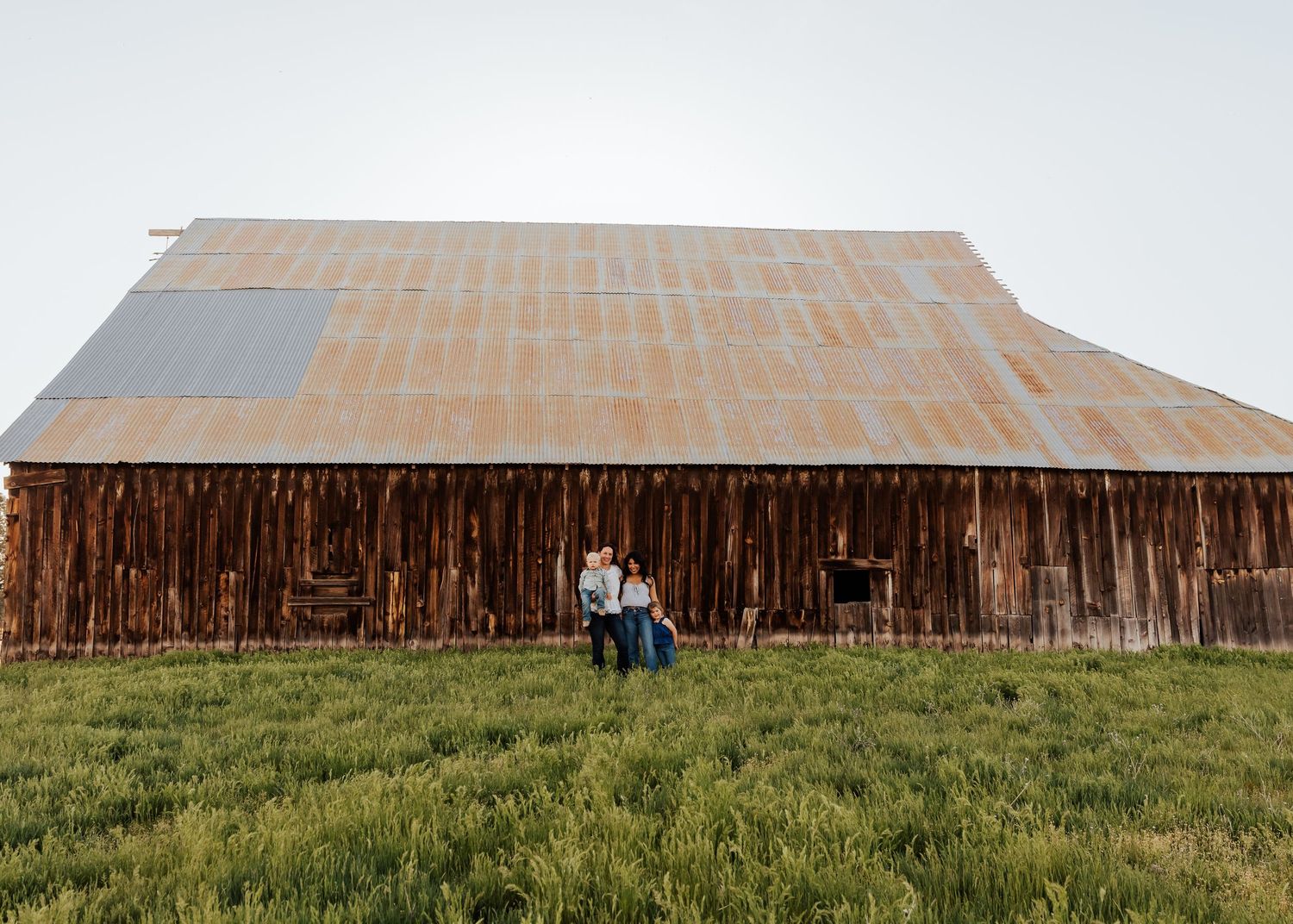 Rustic wooden barn stands against green grass and cloudy sky in rural countryside setting.