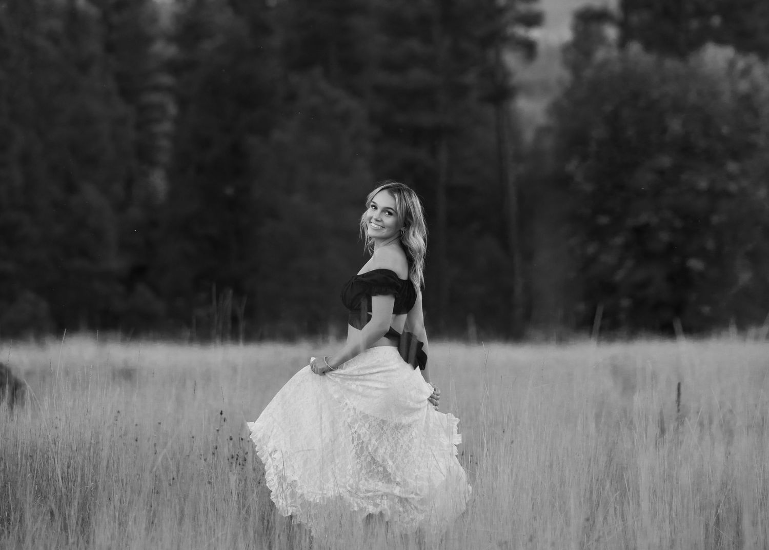 Dramatic black and white portrait in off-shoulder top and flowing skirt in mountain field.