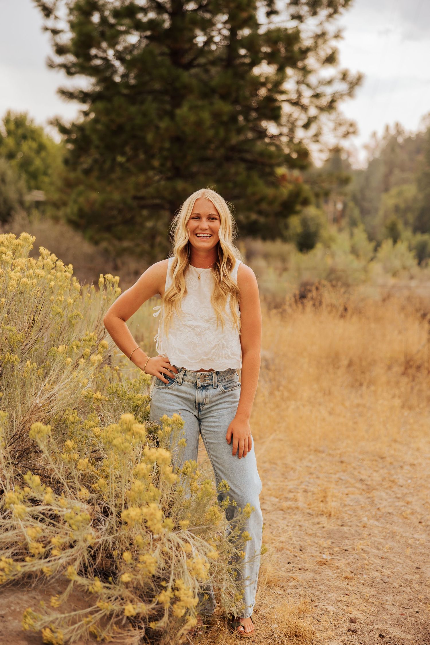 Person in casual outfit posing among yellow wildflowers in natural setting.