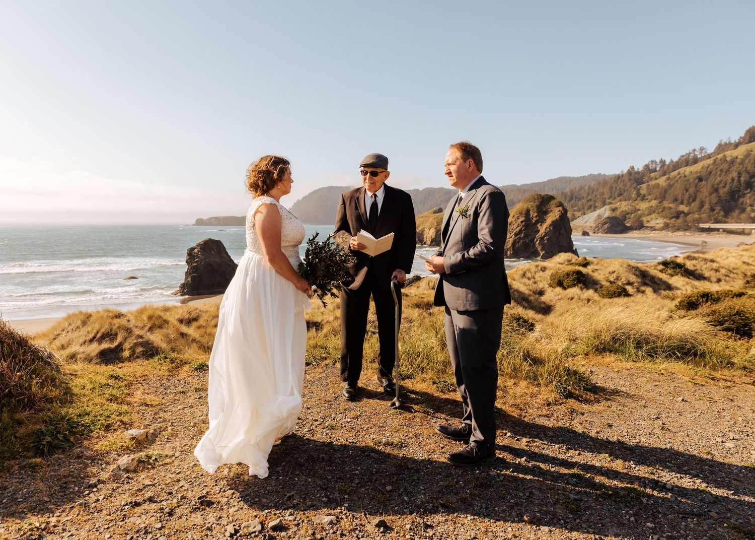 A wedding ceremony takes place on a scenic coastal cliff overlooking the ocean at sunset.