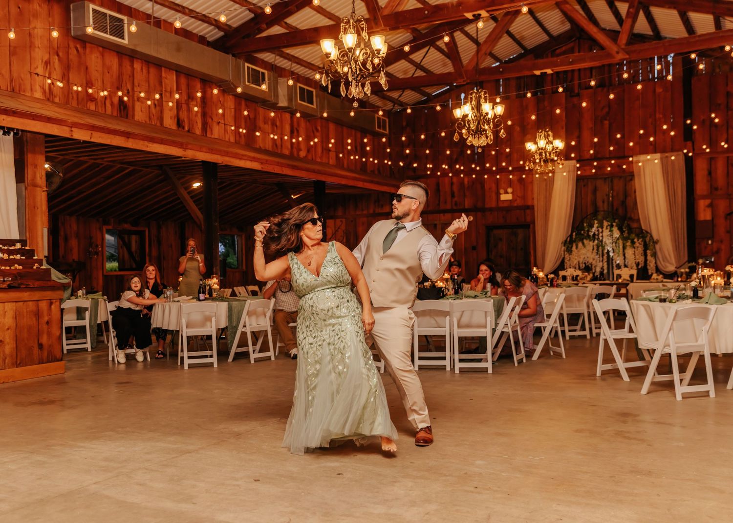 Rustic barn wedding reception venue decorated with hanging chandeliers and string lights.